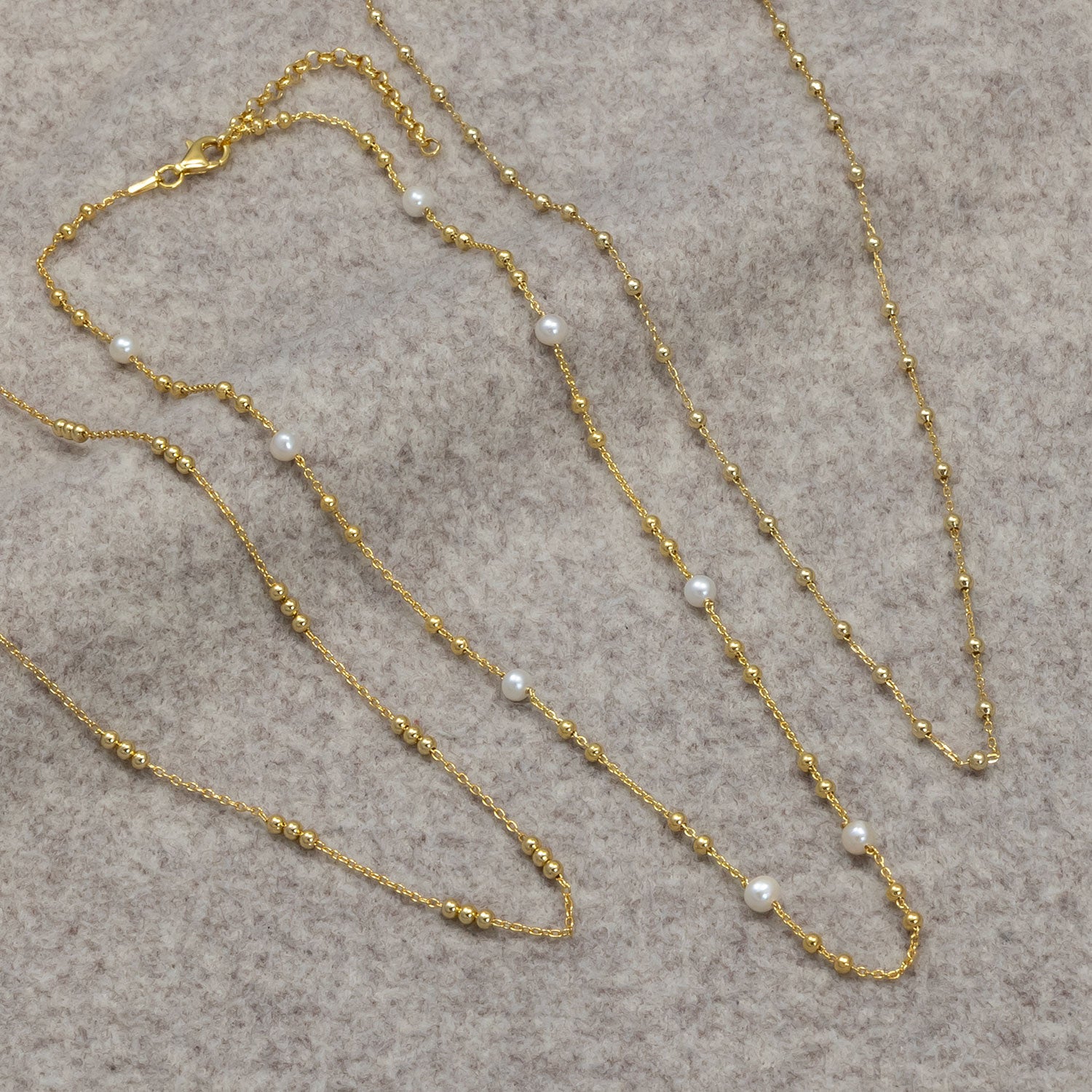 Three delicate gold vermeil bead chain necklaces, two featuring evenly spaced small pearls, displayed on a soft neutral fabric background.
