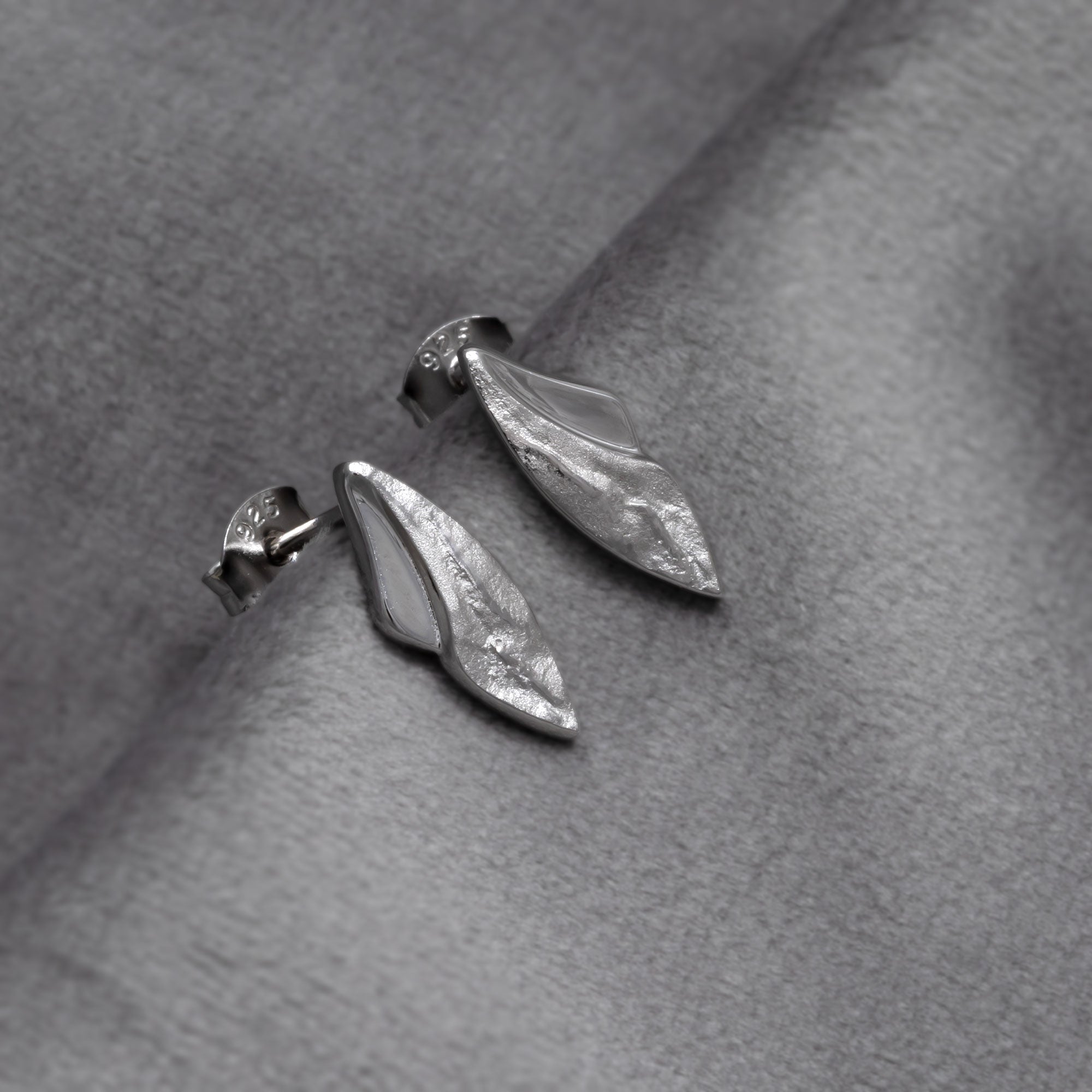 Pair of sterling silver stud earrings featuring a curved design with textured and polished surfaces, showcasing sculptural elegance in contemporary silver jewellery. Placed on a grey velvet cloth.
