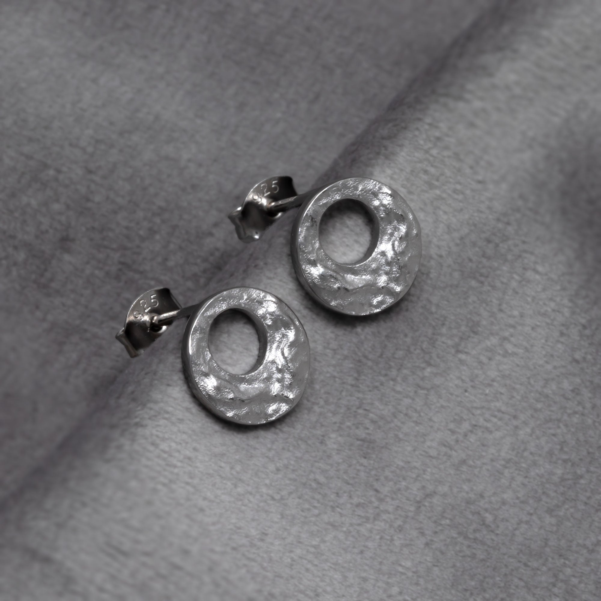 Pair of sterling silver circular stud earrings with a textured surface inspired by natural rock formations, showcasing sculptural elegance in contemporary silver jewellery. Placed on a grey velvet cloth.