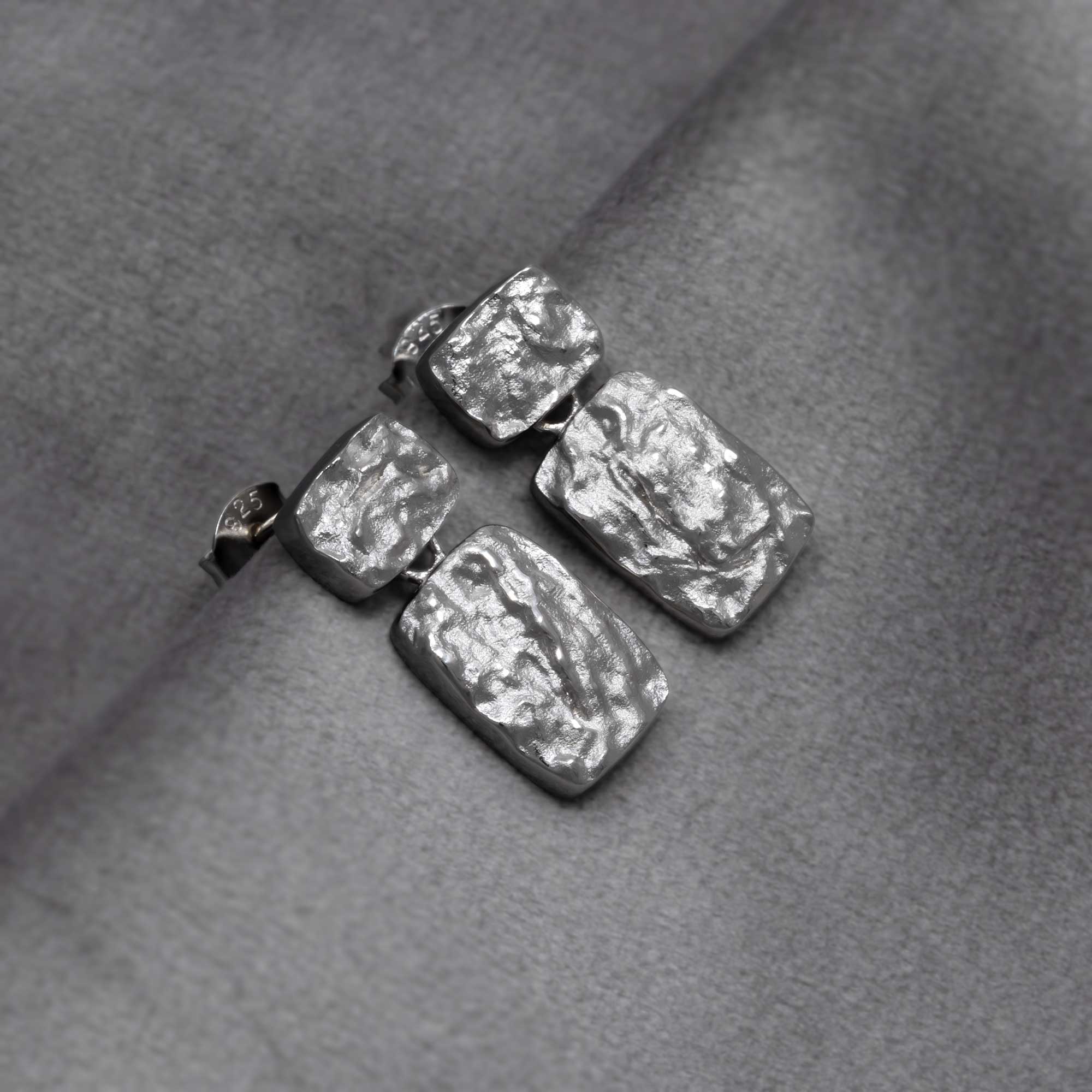 Rectangular drop earrings in polished sterling silver featuring an organic, textured surface with a modern sculptural design for refined British silver jewellery. Placed on a grey velvet cloth.