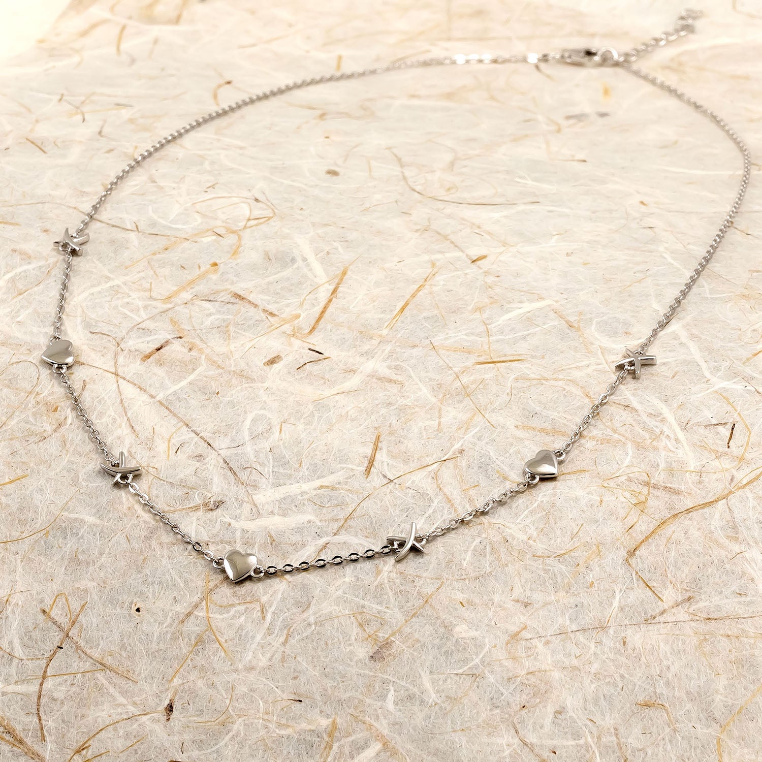 Delicate sterling silver necklace featuring alternating heart and kiss-shaped charms along a fine link chain, embodying modern elegance in British silver jewellery design.