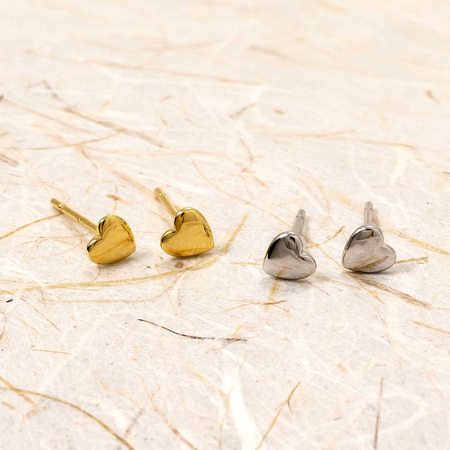 Polished sterling silver and gold vermeil heart-shaped stud earrings with a smooth, sculptural finish, reflecting refined contemporary British silver jewellery design.
