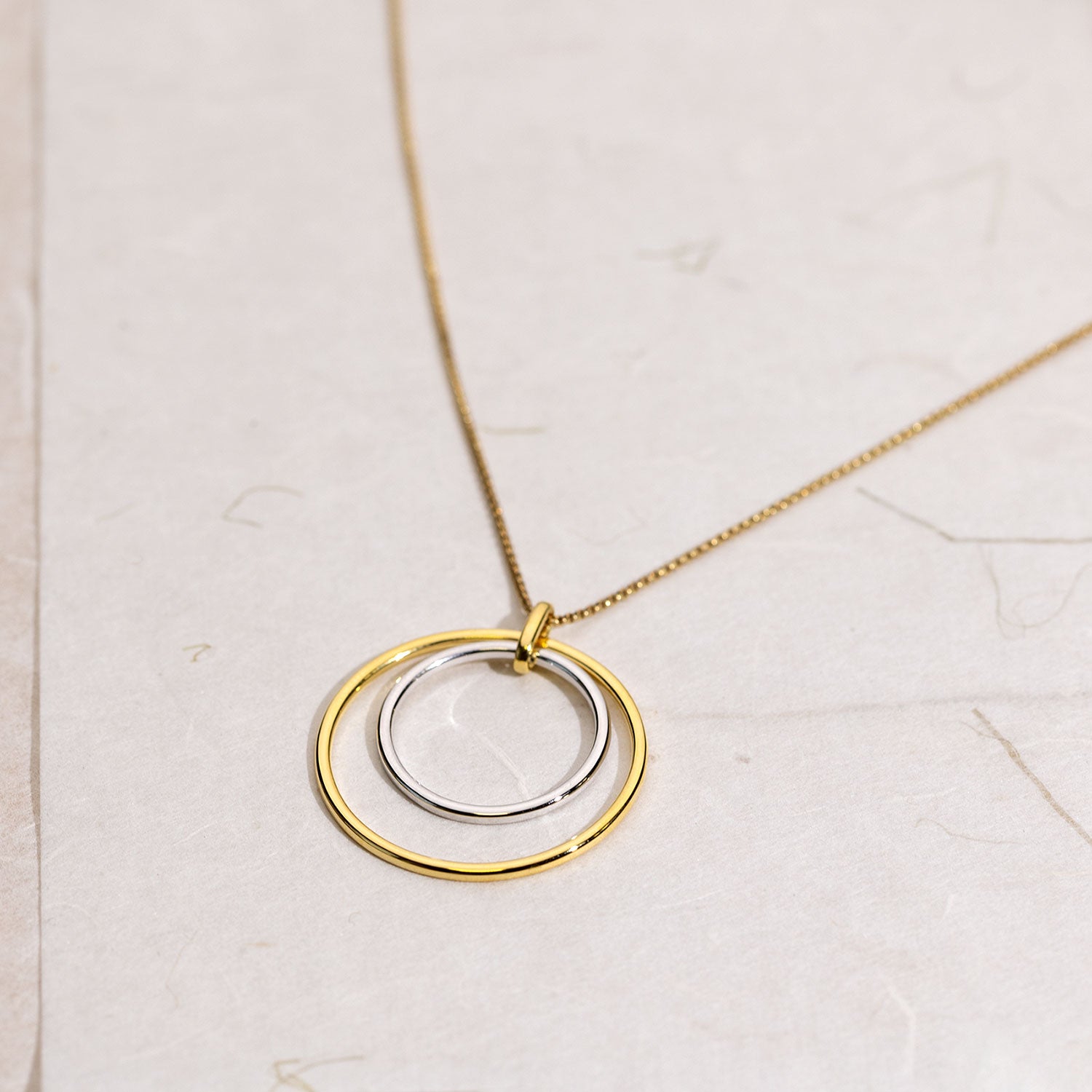 Delicate pendant featuring two interlocking circles crafted in sterling silver and gold vermeil, suspended from a fine chain for a modern, sculptural look.