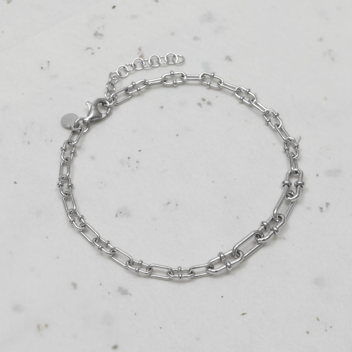 A sterling silver chain link bracelet with a lobster clasp and extension chain, displayed on a textured surface.