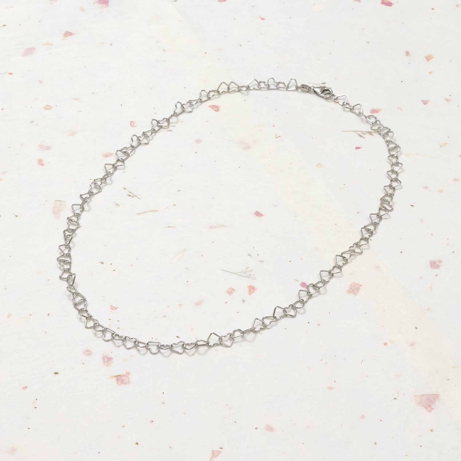 Delicate sterling silver necklace composed of interconnected miniature heart-shaped links, designed for adjustable length and versatile wear.