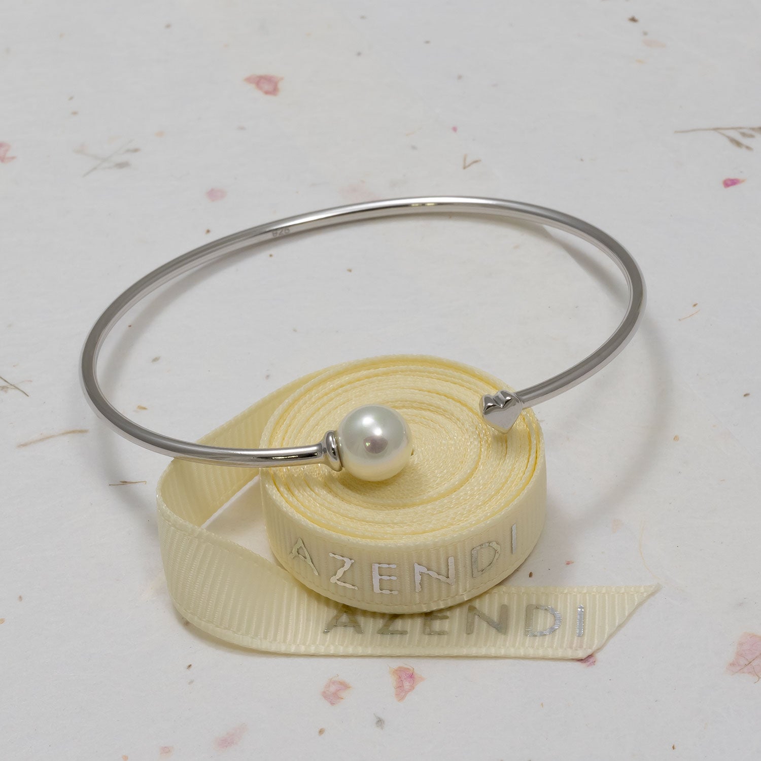 Minimalist sterling silver flexi cuff featuring a lustrous shell pearl and small heart detail, embodying refined British design in contemporary silver jewellery.