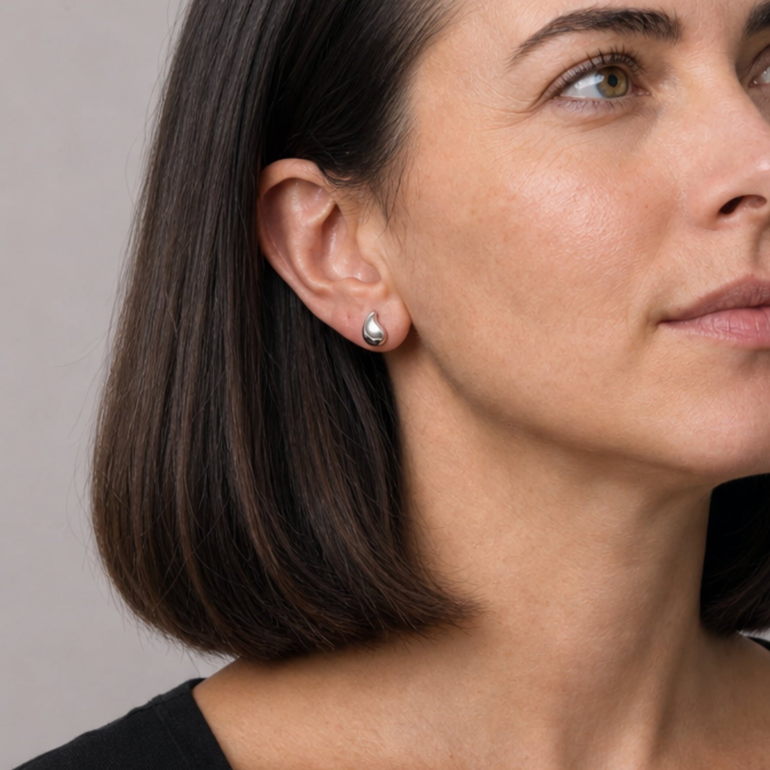 Model wears a pair of sterling silver stud earrings with a satin and polished finish, shaped as elegant teardrops to create a refined and contemporary look in silver jewellery.