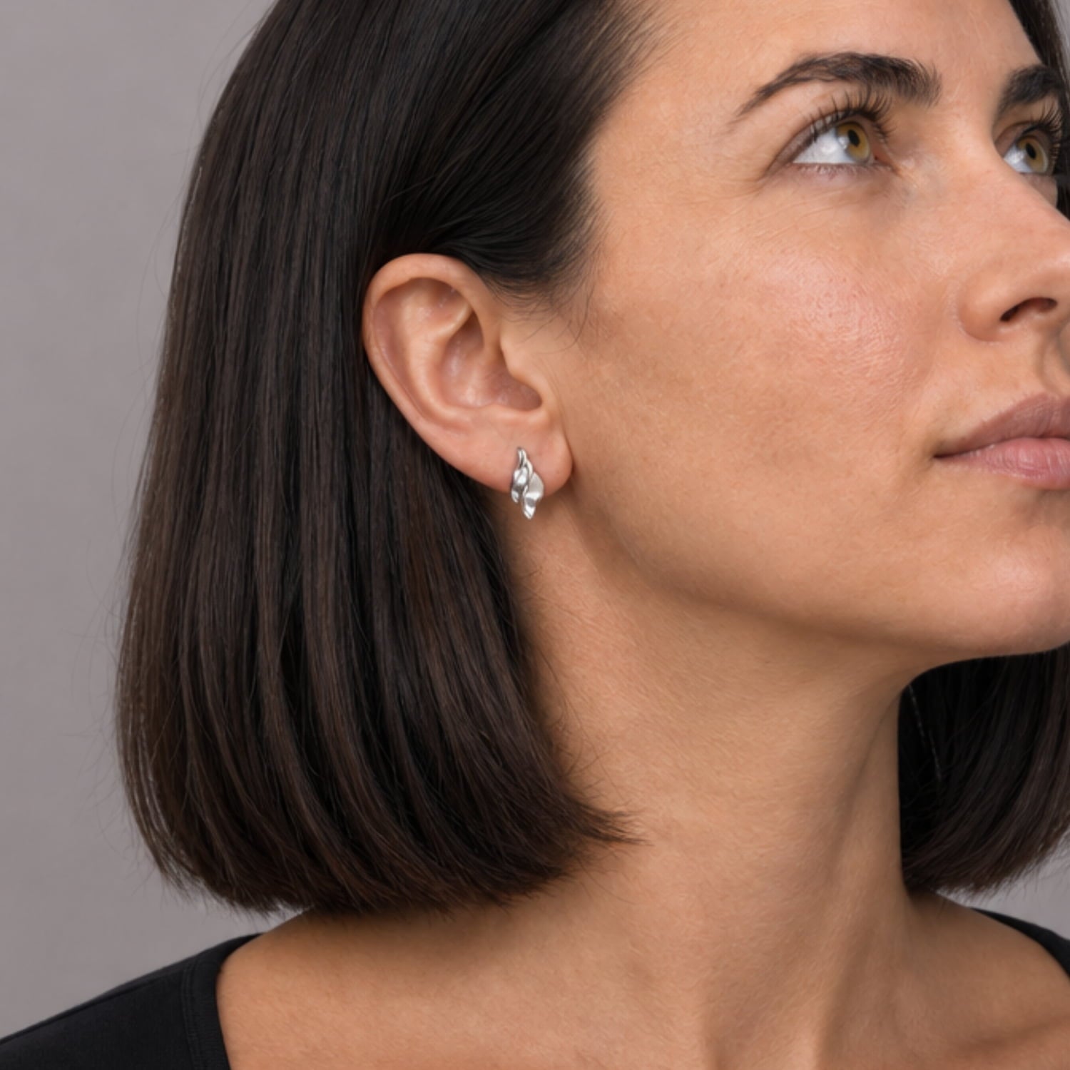 Model wears a pair of sterling silver stud earrings with a double wave design combining satin and polished finishes, offering a refined sculptural look in contemporary silver jewellery.