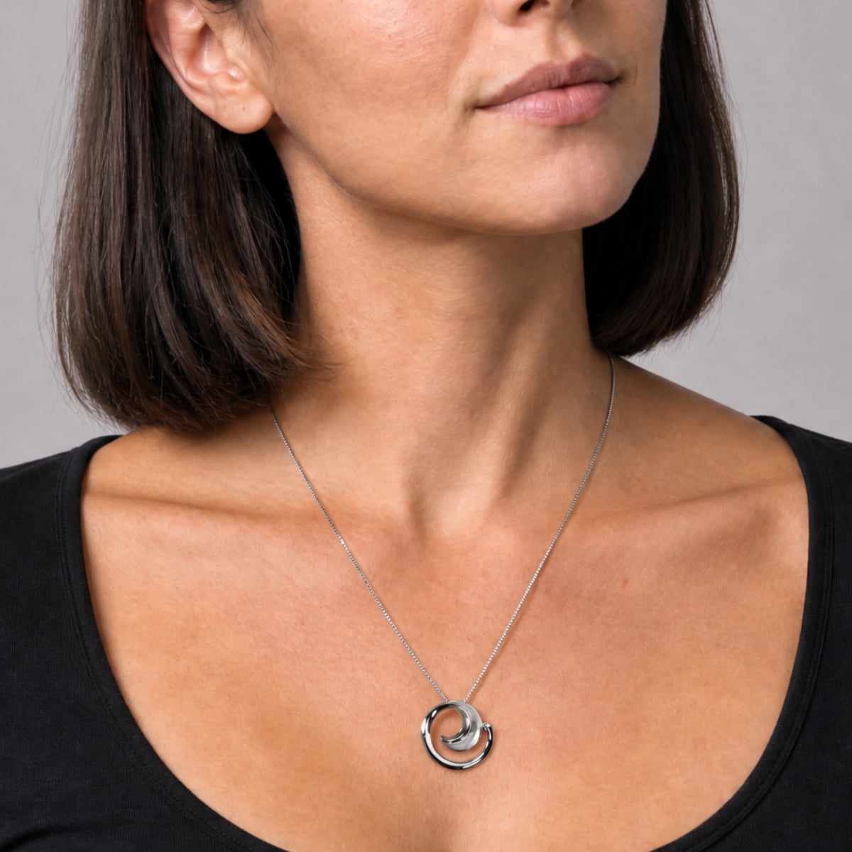 A close-up of a woman wearing curling polished and satin pendant, styled with a black top against a neutral gray background.
