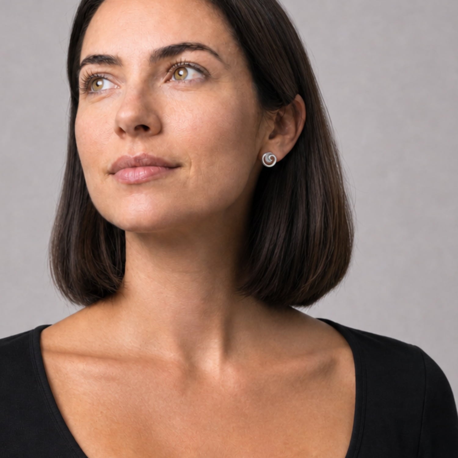 Model wears a pair of sterling silver stud earrings featuring a curling, satin and polished design with a fluid, sculptural form for refined contemporary silver jewellery by Azendi.