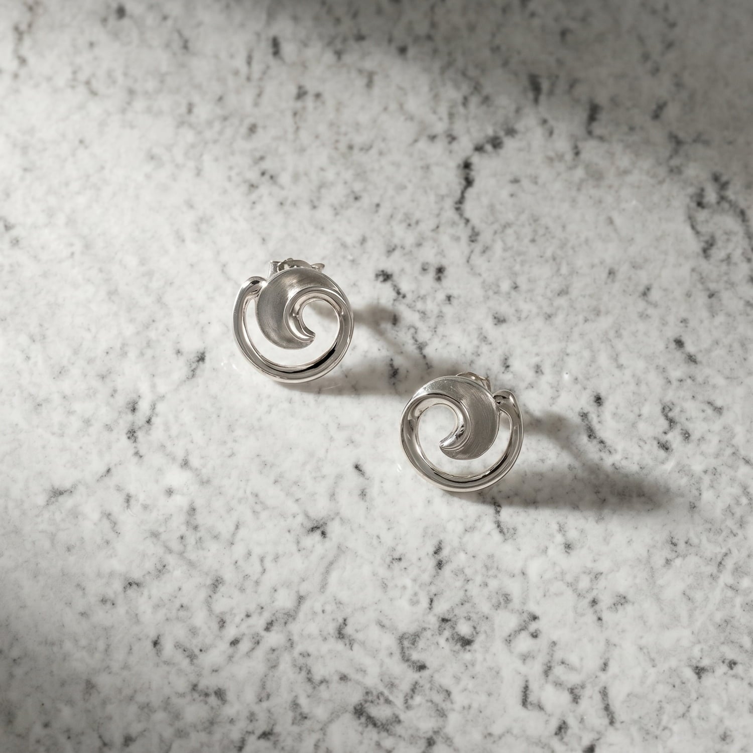 Pair of sterling silver stud earrings featuring a satin and polished finish with an elegant curling design, reflecting refined contemporary silver jewellery by Azendi.