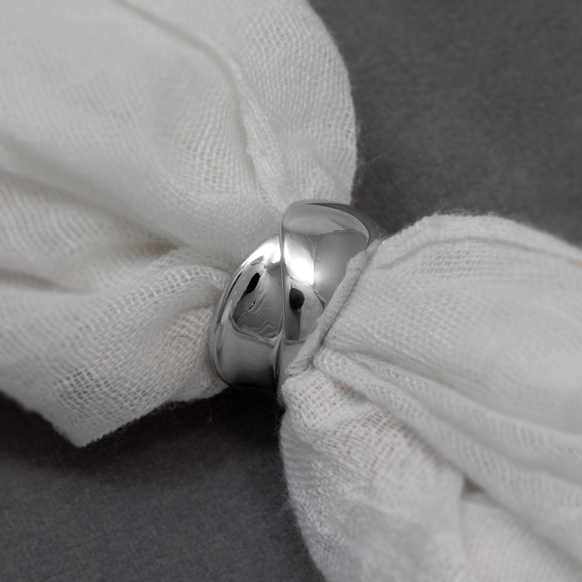 Polished sterling silver ring featuring a sculptural twisting ribbon design with smooth, reflective surfaces in a contemporary style. Threaded on a white cloth laid on a grey velvet fabric.