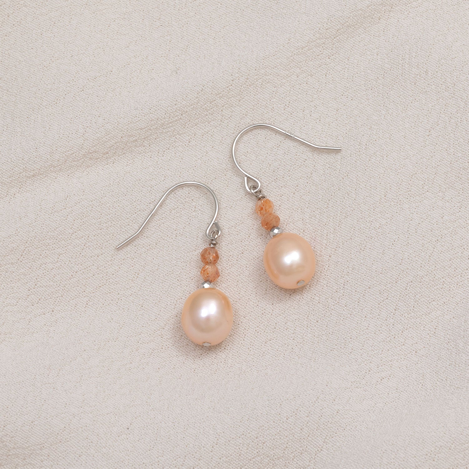 Sterling silver earrings featuring luminous freshwater pearls paired with faceted sunstone beads, creating an elegant and sculptural design in fine silver jewellery.