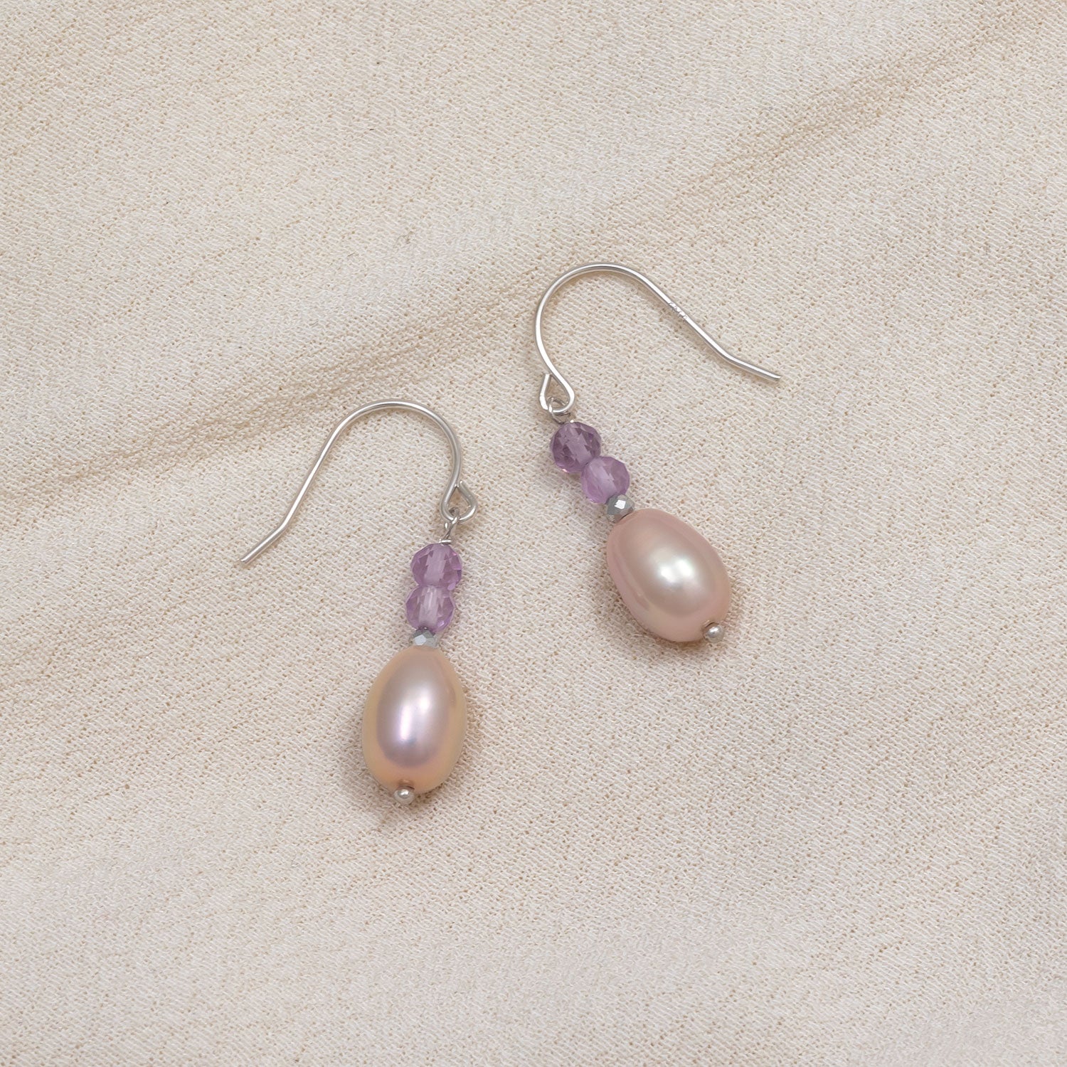Sterling silver drop earrings featuring smooth freshwater pearls paired with faceted amethyst beads, offering a delicate and elegant design with subtle color contrast.