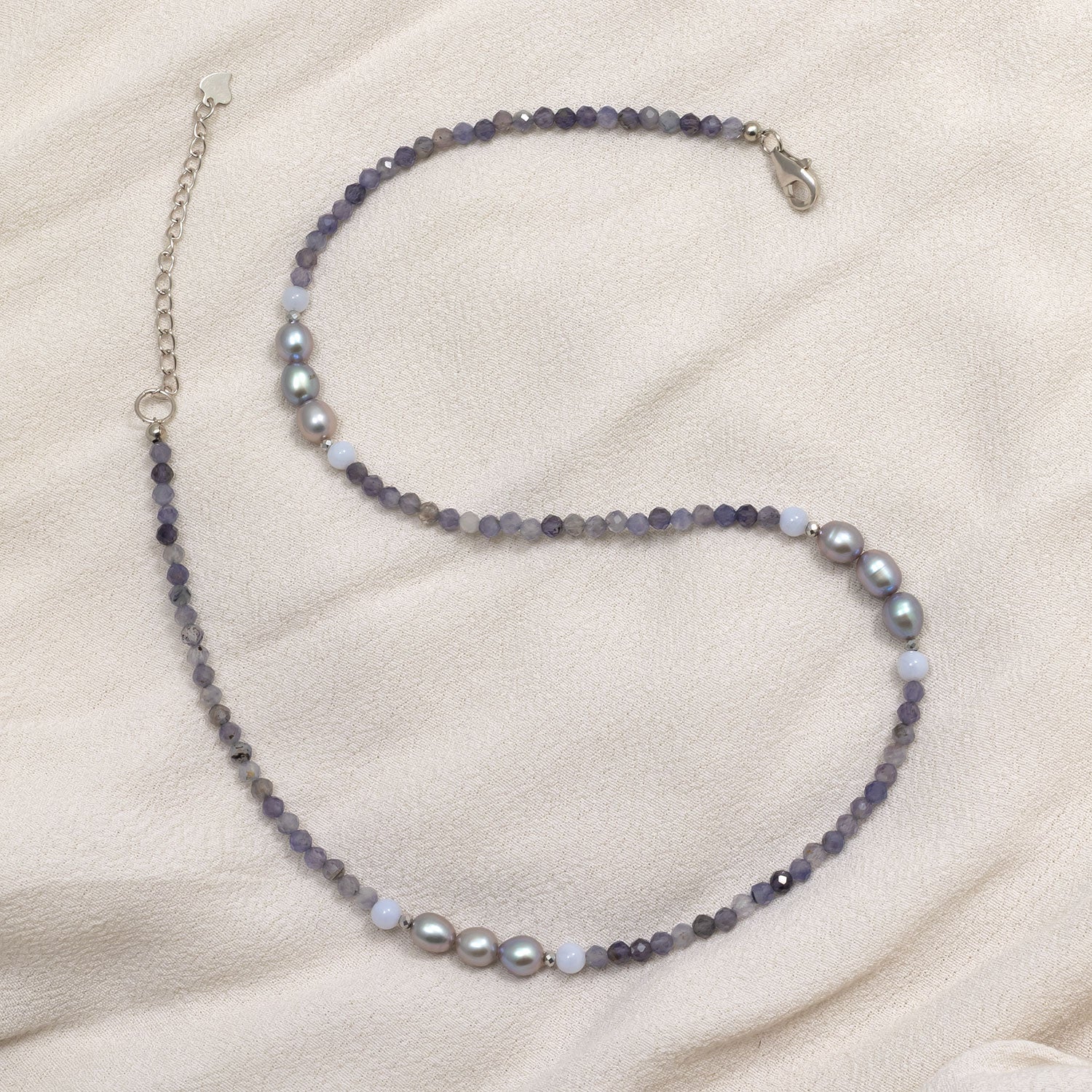 Delicate necklace featuring faceted iolite beads interspersed with lustrous freshwater pearls and small pale gemstone accents, secured with a sterling silver clasp on a soft fabric background.