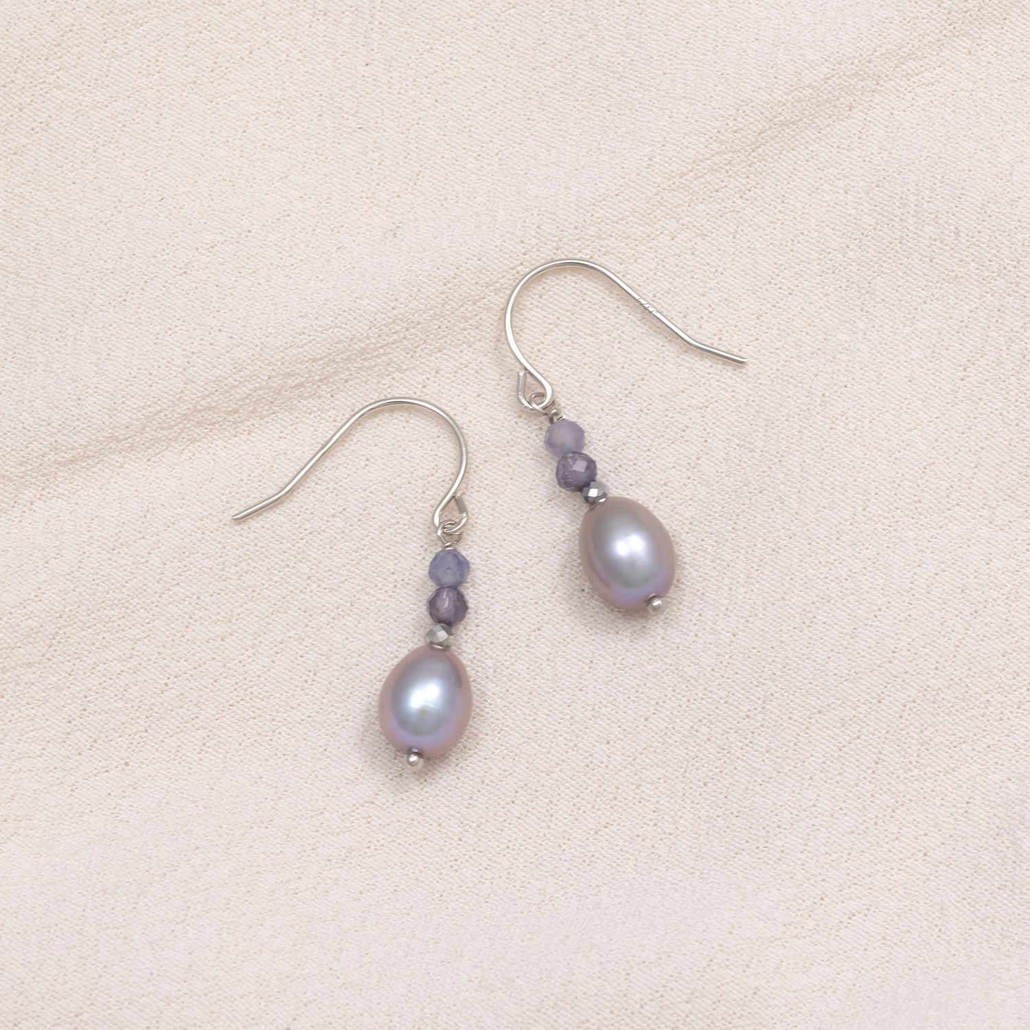 Sterling silver drop earrings featuring luminous freshwater pearls paired with faceted iolite beads, combining elegant natural gemstones in a refined, contemporary design.