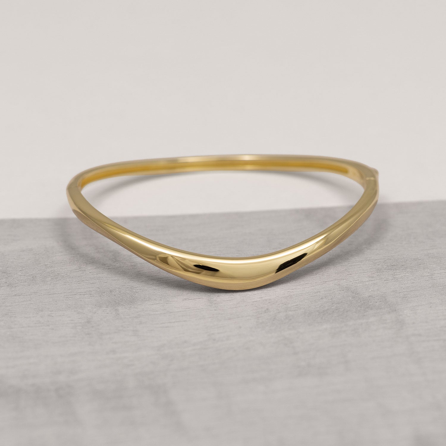 Sleek gold vermeil bangle featuring a slim wave design with a hinged closure, combining minimalist elegance with contemporary British craftsmanship.