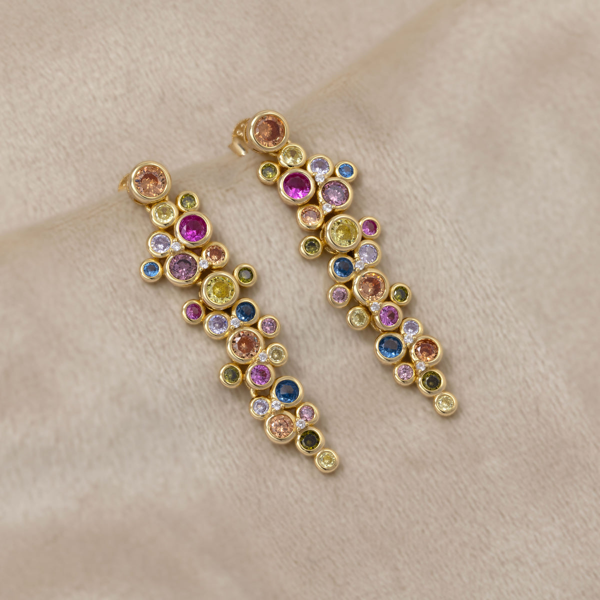 Gold vermeil drop earrings featuring a cluster of colorful bubble-like gemstones in varied hues for a vibrant, sculptural look. Placed on a cream velvet cloth.