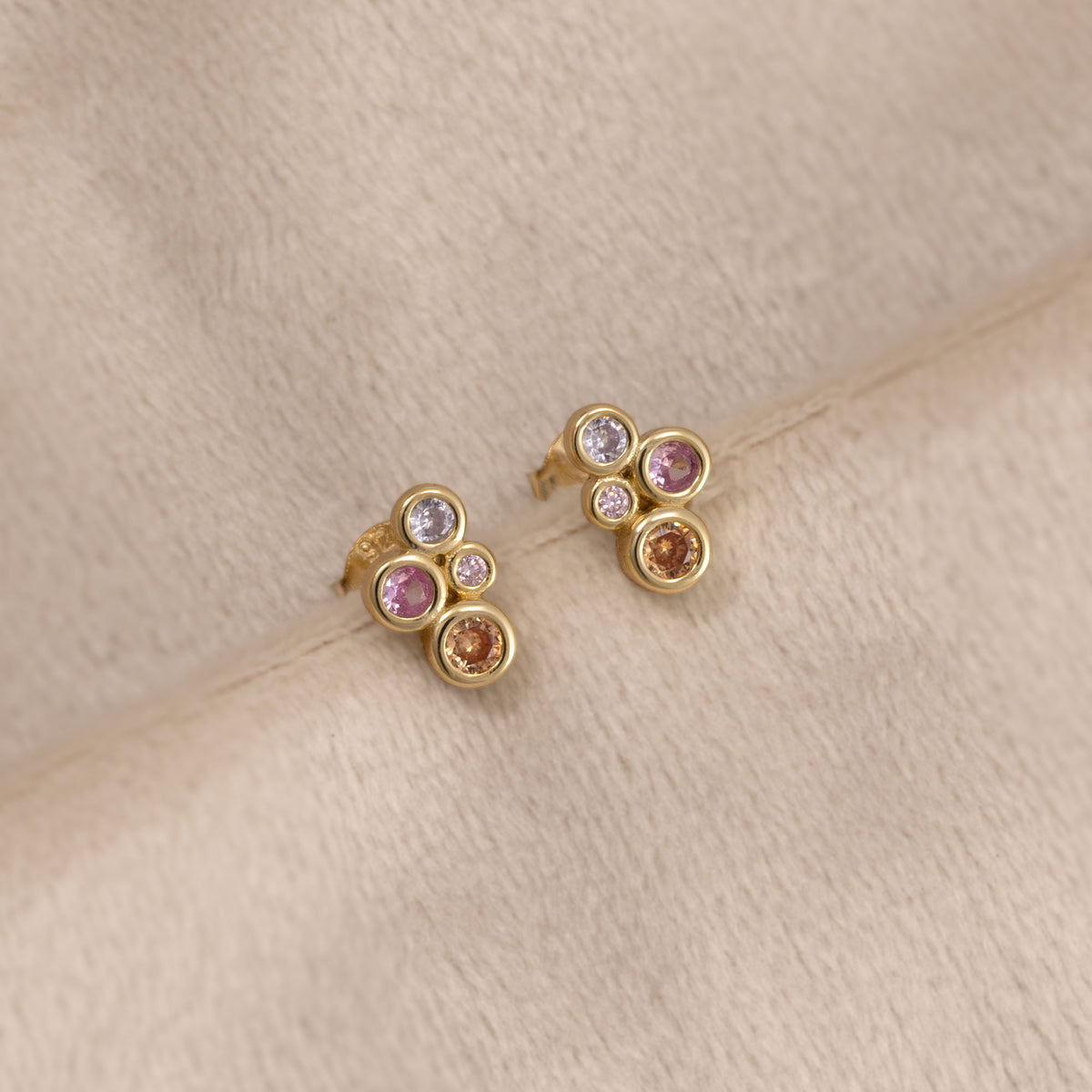 Pair of gold vermeil stud earrings featuring colourful pink, purple, and orange bubble-shaped gemstones in a sculptural cluster design by Azendi. Placed on a cream velvet cloth.