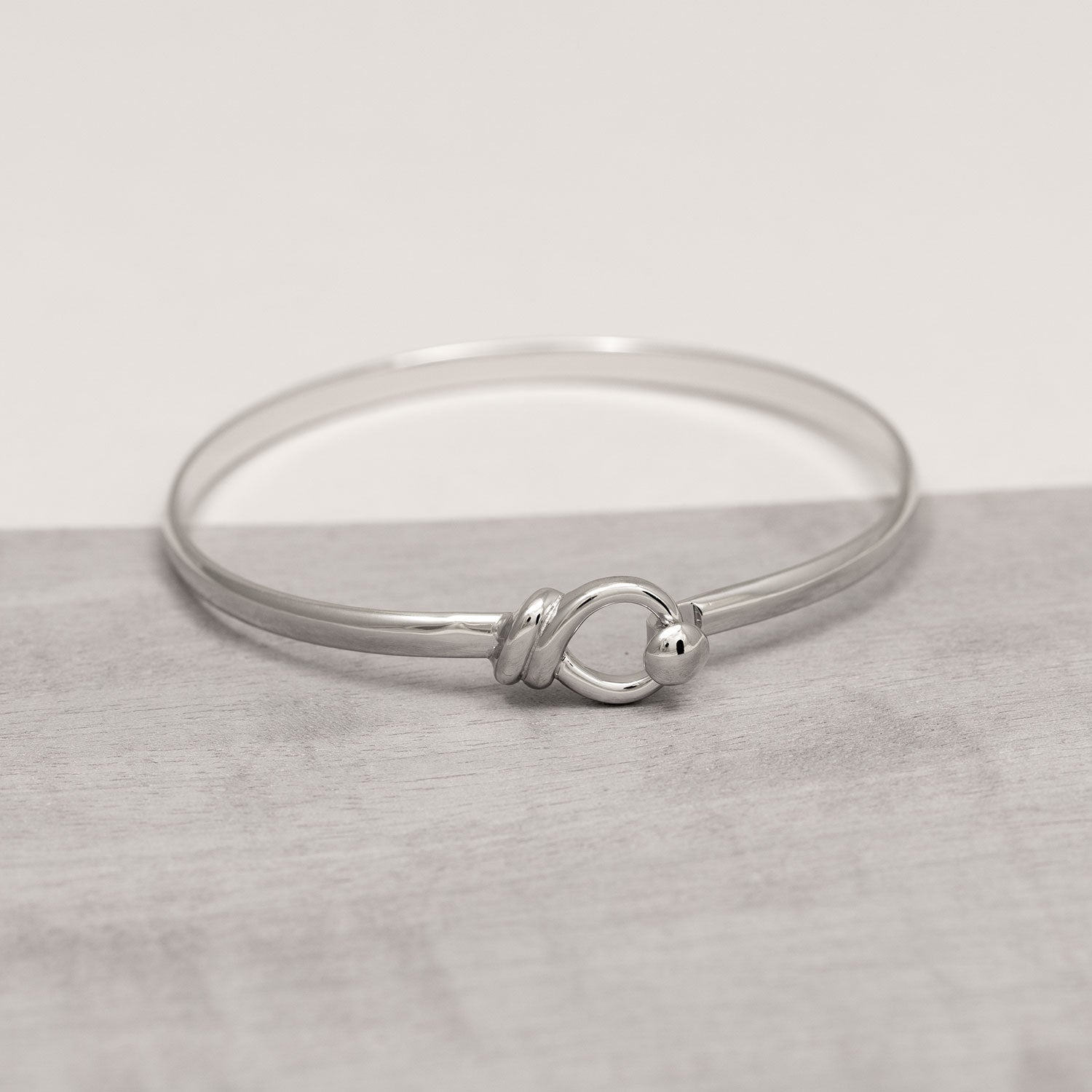 Slim sterling silver bangle featuring a sculptural looping hook detail, exemplifying sleek, contemporary British design in fine silver jewellery.