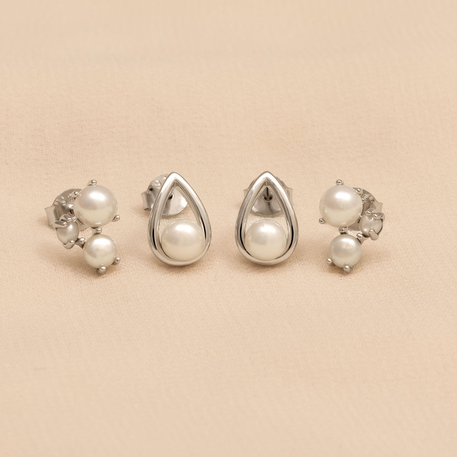 Pair of sterling silver stud earrings featuring lustrous freshwater pearls, with one design framed in a sleek teardrop shape and the other showcasing clustered pearl accents.