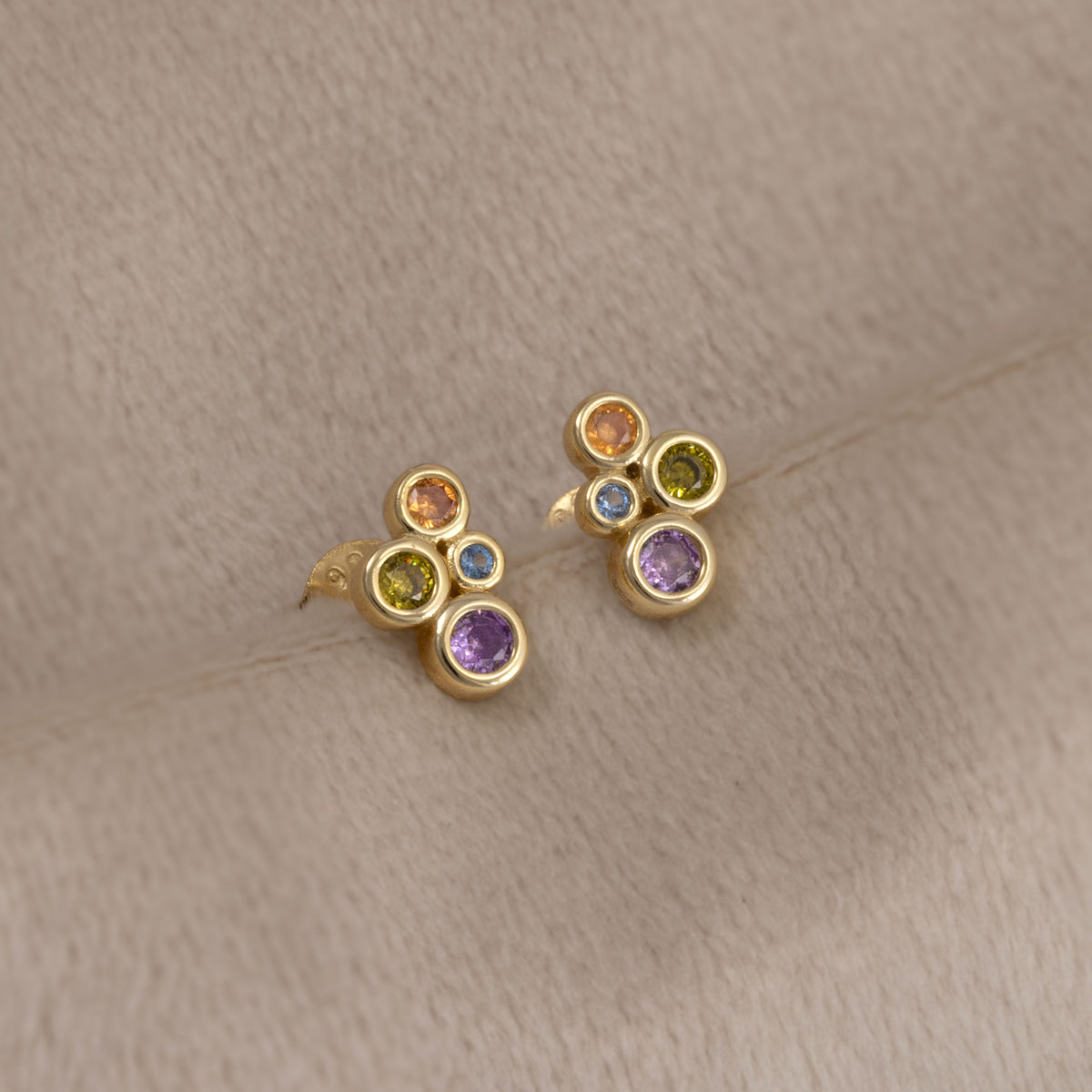 Pair of gold vermeil stud earrings featuring clusters of colourful purple and green bubble-shaped gemstones. Placed on a cream velvet cloth.