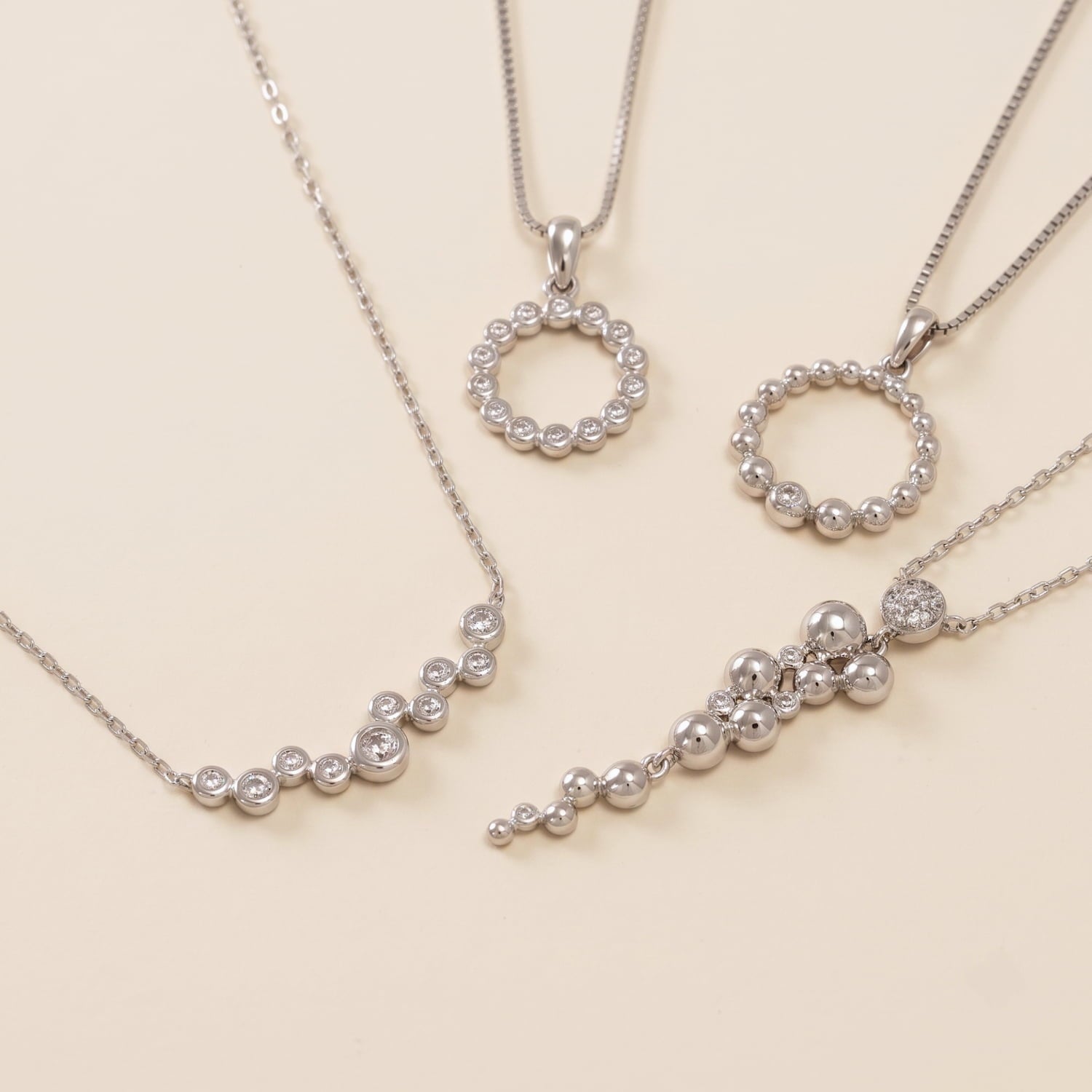 Collection of contemporary sterling silver necklaces featuring various sculptural bead and cubic zirconia designs on delicate chains displayed on a cream surface.