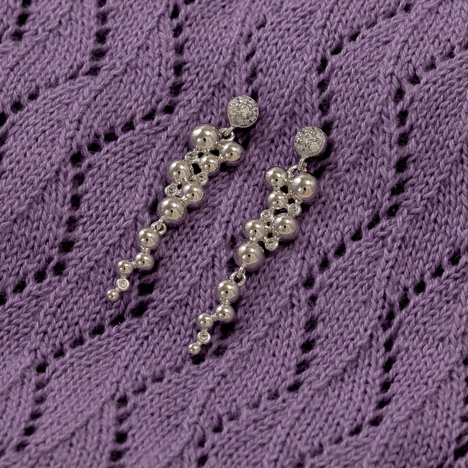 Pair of silver drop earrings featuring cascading polished beads accented with sparkling cubic zirconia studs, displayed on textured purple fabric, exemplifying refined sterling silver craftsmanship.