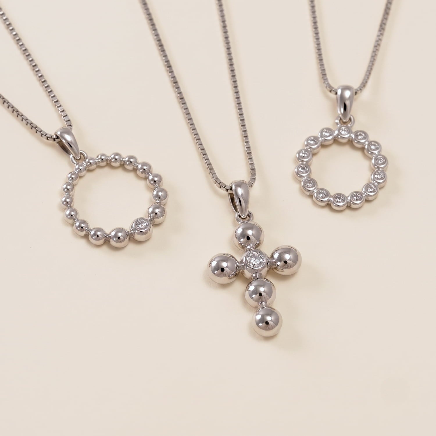 Collection of contemporary sterling silver necklaces featuring various sculptural bead and cubic zirconia designs on delicate chains displayed on a cream surface.