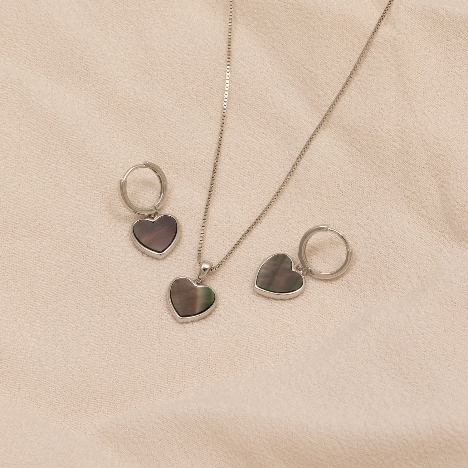 Delicate sterling silver hoop earrings and matching necklace pendant featuring grey mother of pearl heart charms, showcasing sculptural elegance in silver jewellery by Azendi.