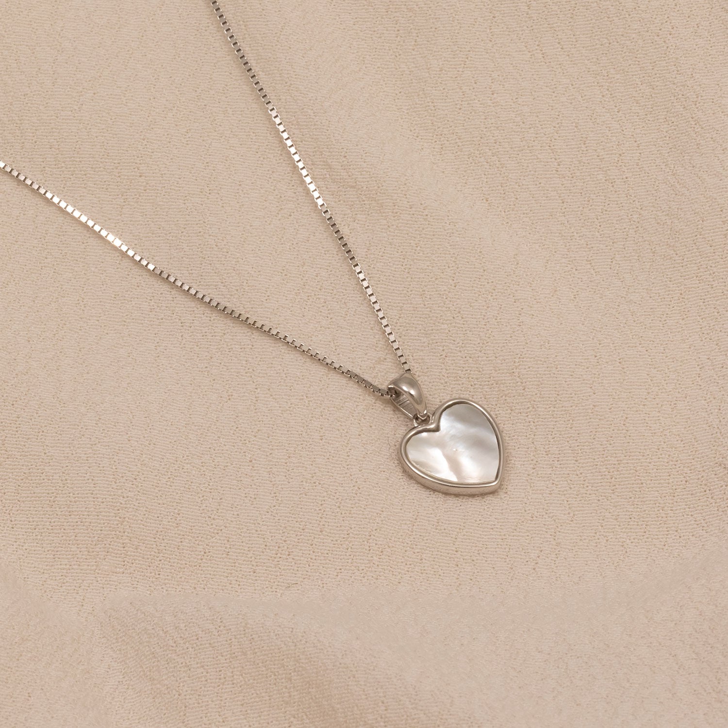 Delicate sterling silver necklace featuring a heart-shaped pendant with a smooth white mother of pearl inlay, showcased on a fine chain against a neutral fabric background.