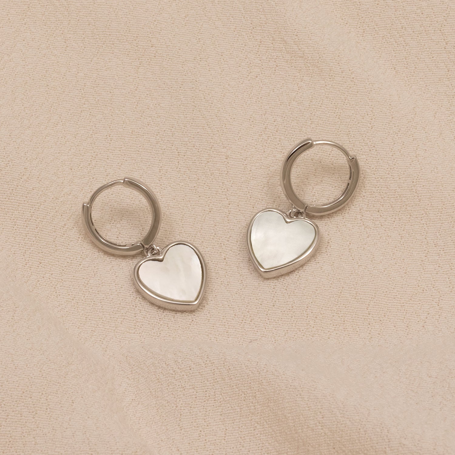 Pair of sterling silver hoop earrings featuring white mother of pearl heart-shaped charms, showcasing a refined and sculptural design in contemporary silver jewellery by Azendi.