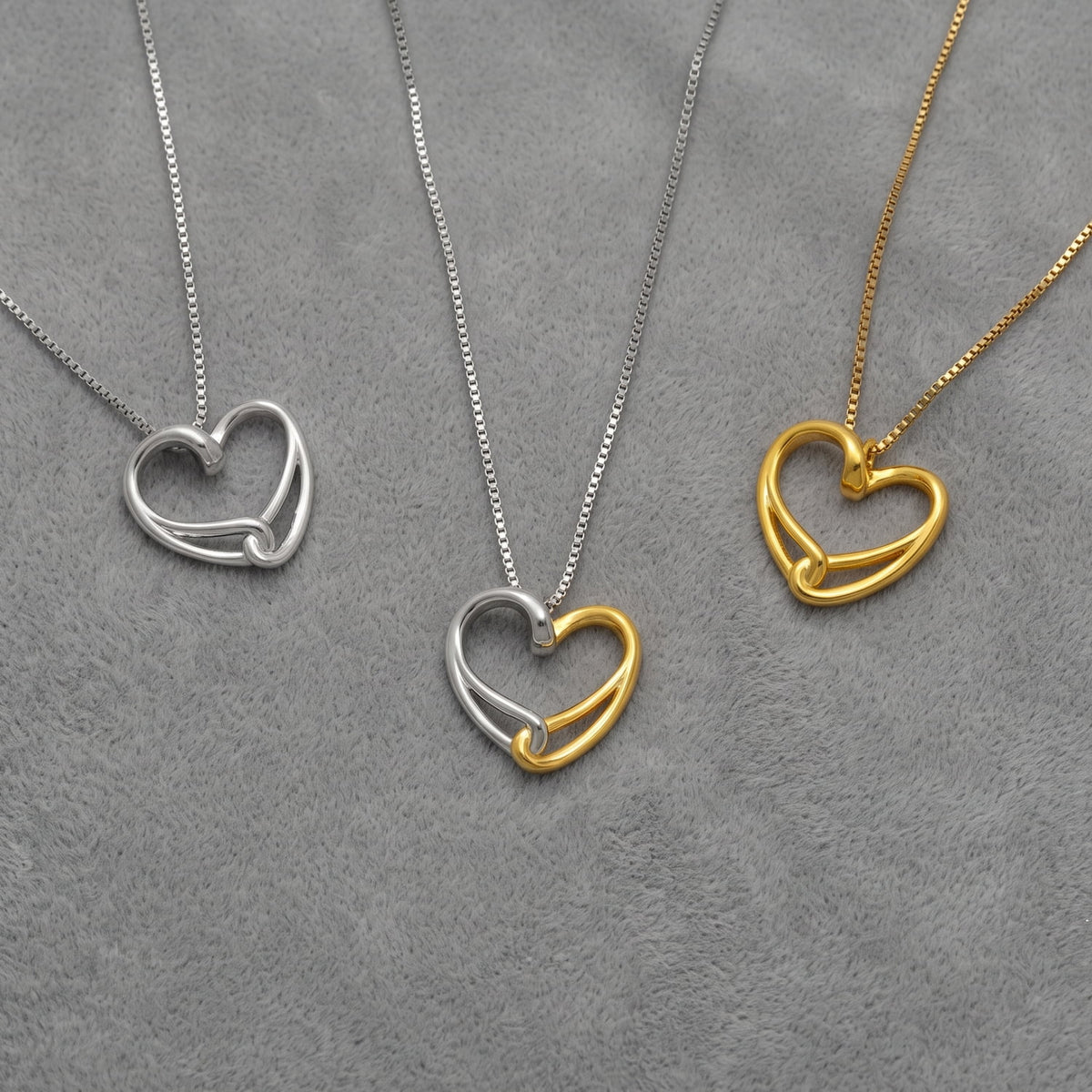 Three heart-shaped pendant necklaces on silver and gold vermeil chains, displayed on a textured gray background.