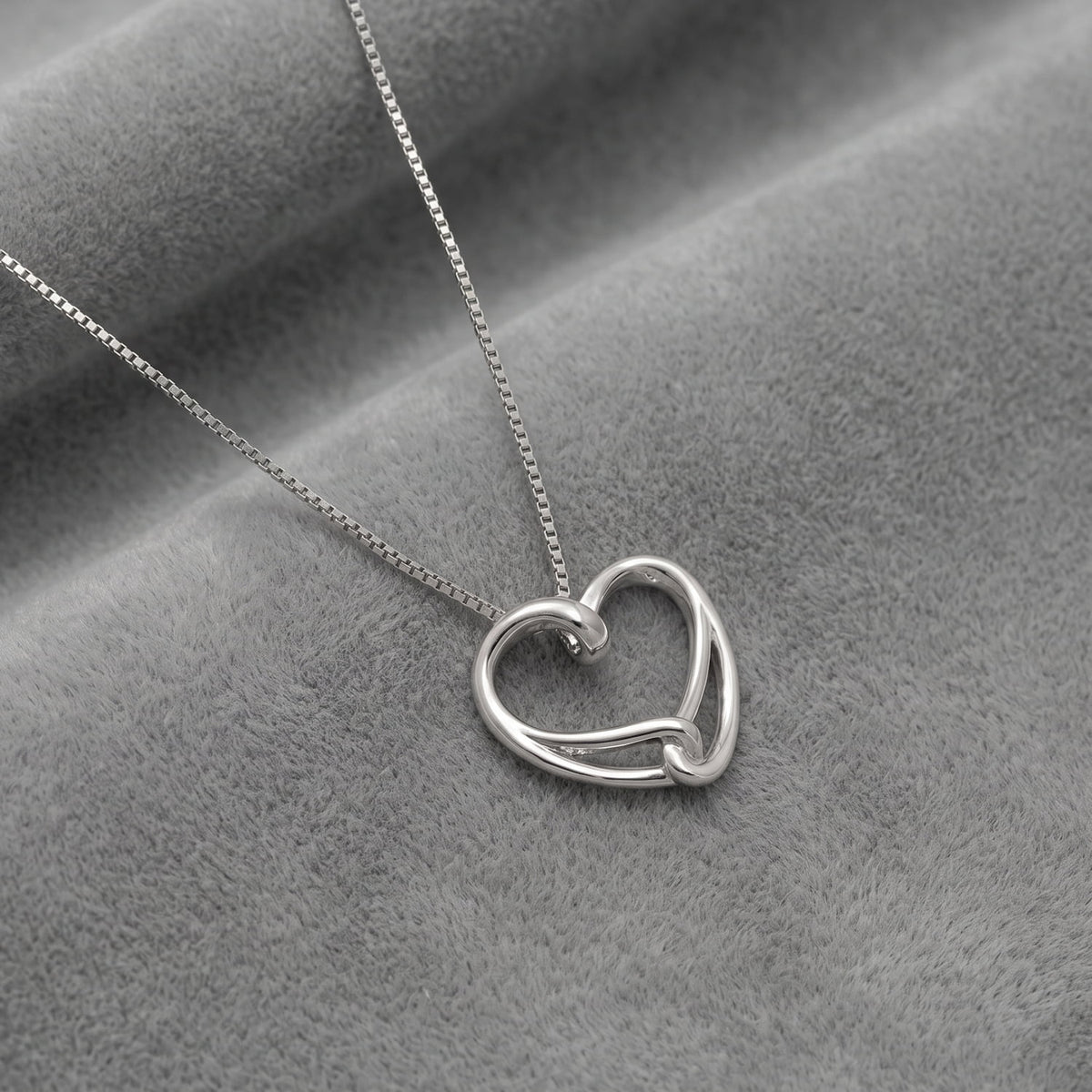 A silver necklace with a double interlocking heart pendant on a delicate chain, displayed on a textured gray fabric background.