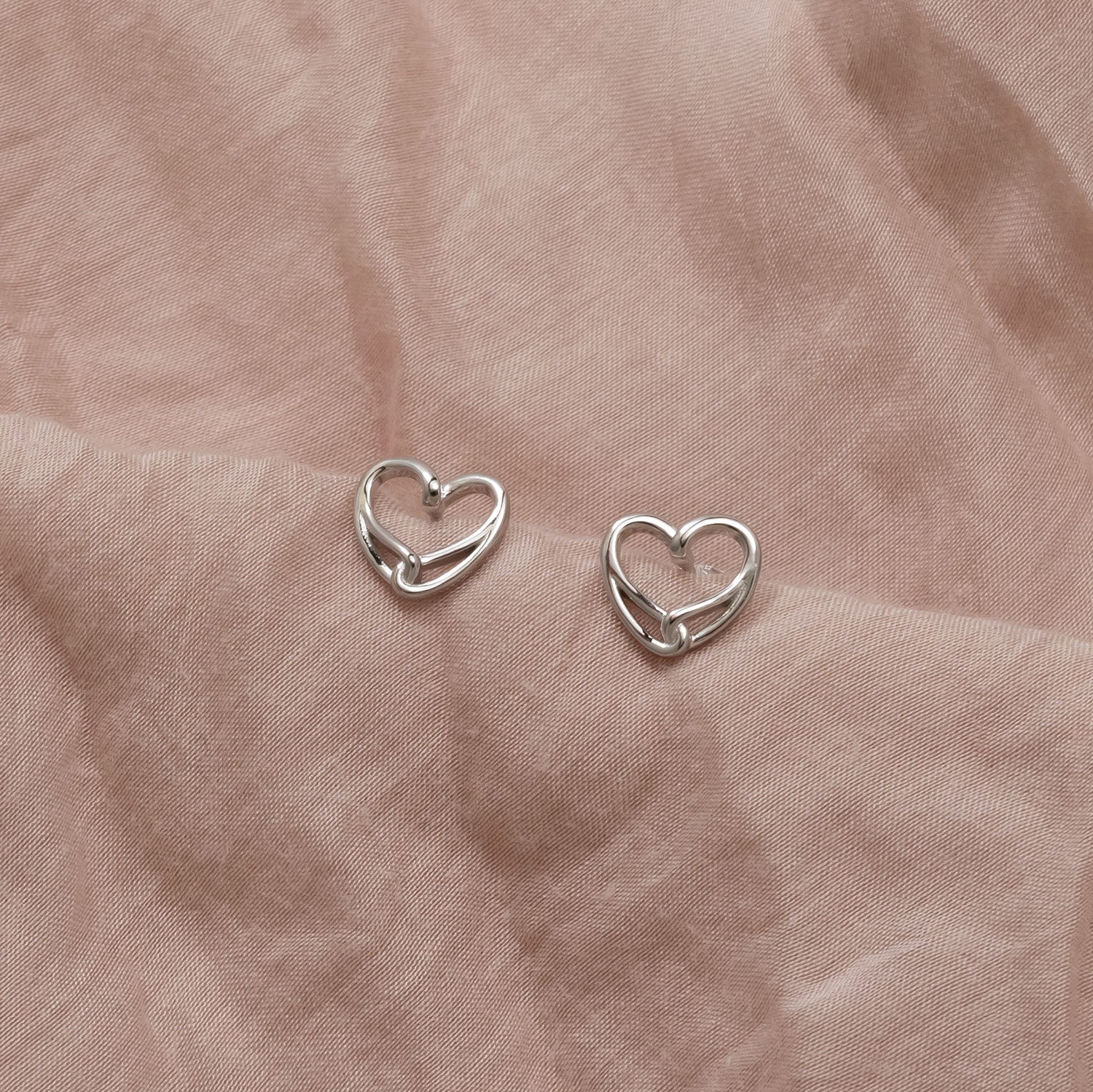 Pair of delicate sterling silver stud earrings featuring an openwork intertwined heart design, showcasing elegant contemporary silver jewellery by Azendi.