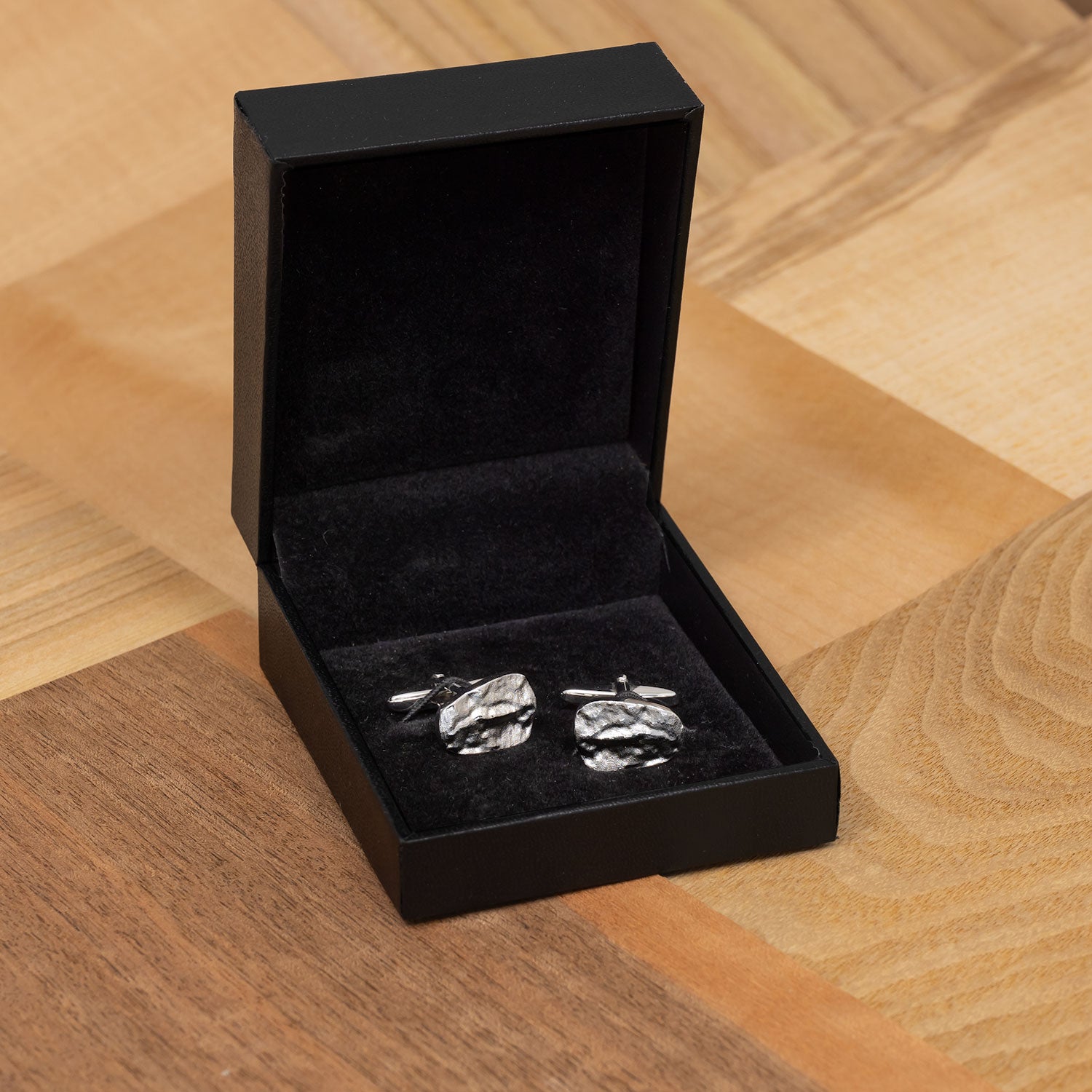 Pair of sterling silver cufflinks inspired by natural pebble textures, presented in a sleek black box, showcasing refined sculptural detail and contemporary British design.