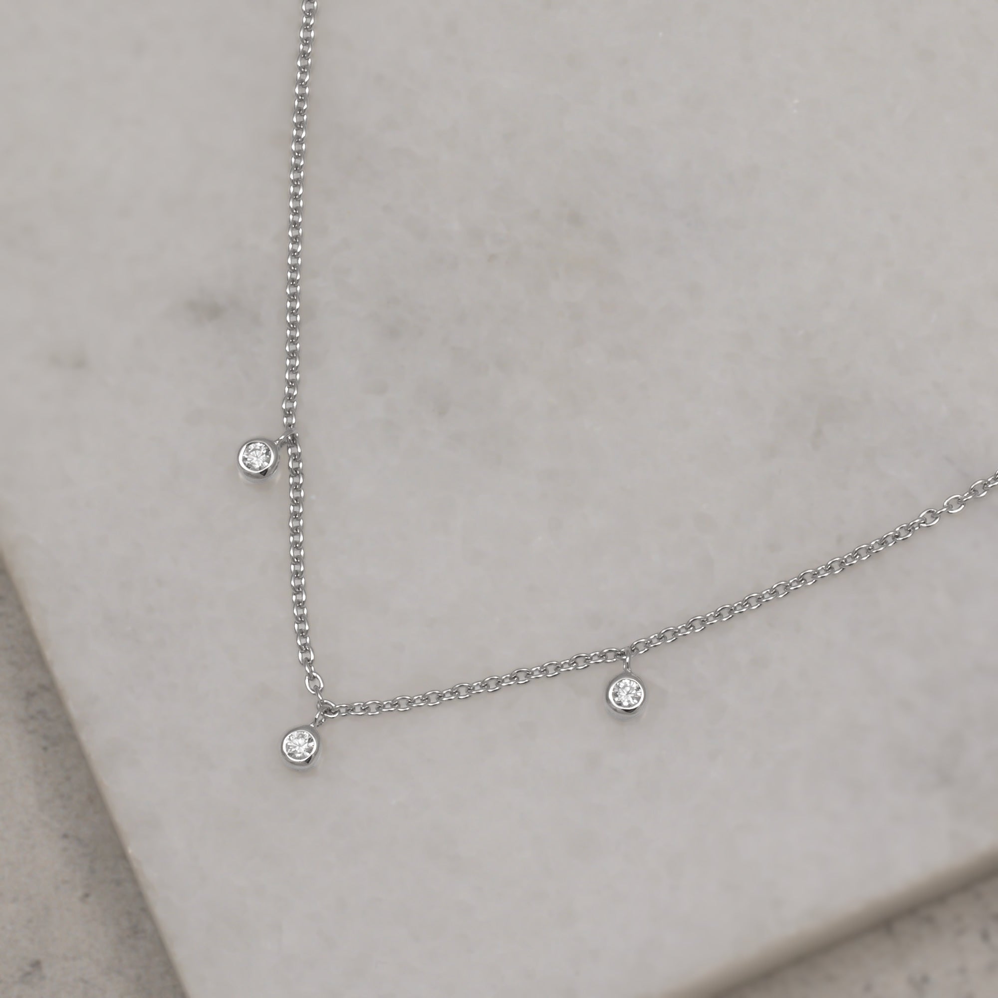 Delicate sterling silver necklace featuring three small gemstone accents suspended along a fine chain with an adjustable extension for versatile wear. Placed on a white quart tile.