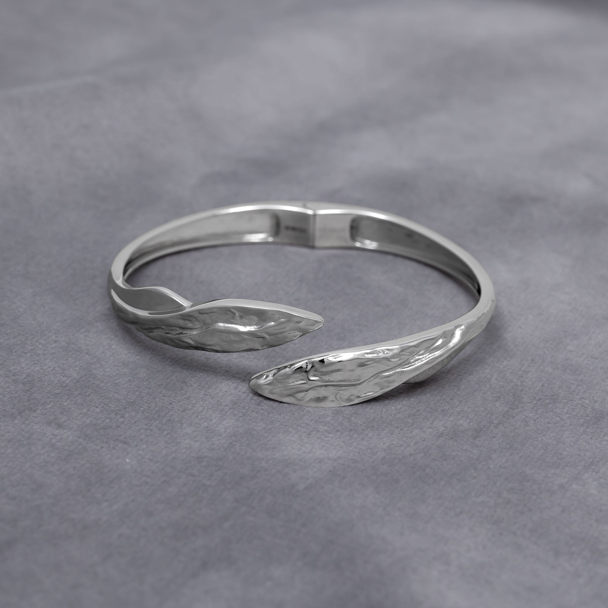 Curved sterling silver hinged bangle featuring a textured and polished finish with sculptural leaf-shaped ends, exemplifying refined contemporary silver jewellery by Azendi. Placed on a grey velvet cloth.