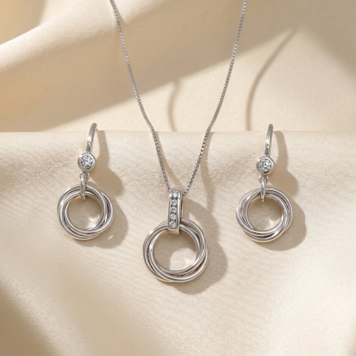 Sterling silver pendant and matching earrings featuring intertwined circular loops with sparkling lab grown diamond accents, showcasing refined sculptural elegance in silver jewellery.
