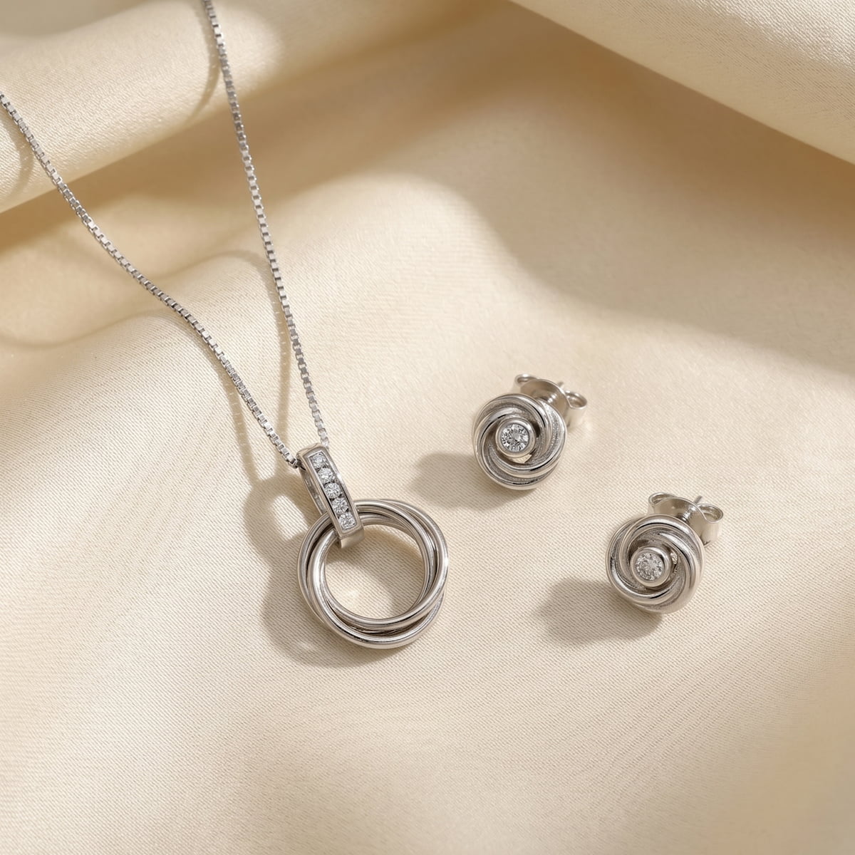Sterling silver necklace and matching stud earrings featuring intertwined loops with sparkling lab grown diamond accents, embodying modern British silver jewellery design.
