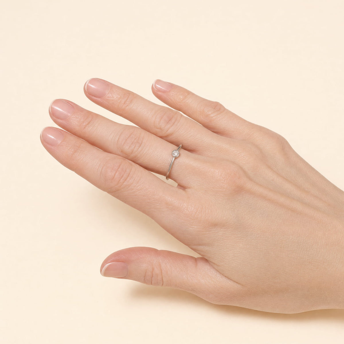 A close up of a model's hand wearing a minimalist sterling silver ring featuring a bezel-set lab grown diamond solitaire, showcasing a sleek and contemporary design from a British jeweller.