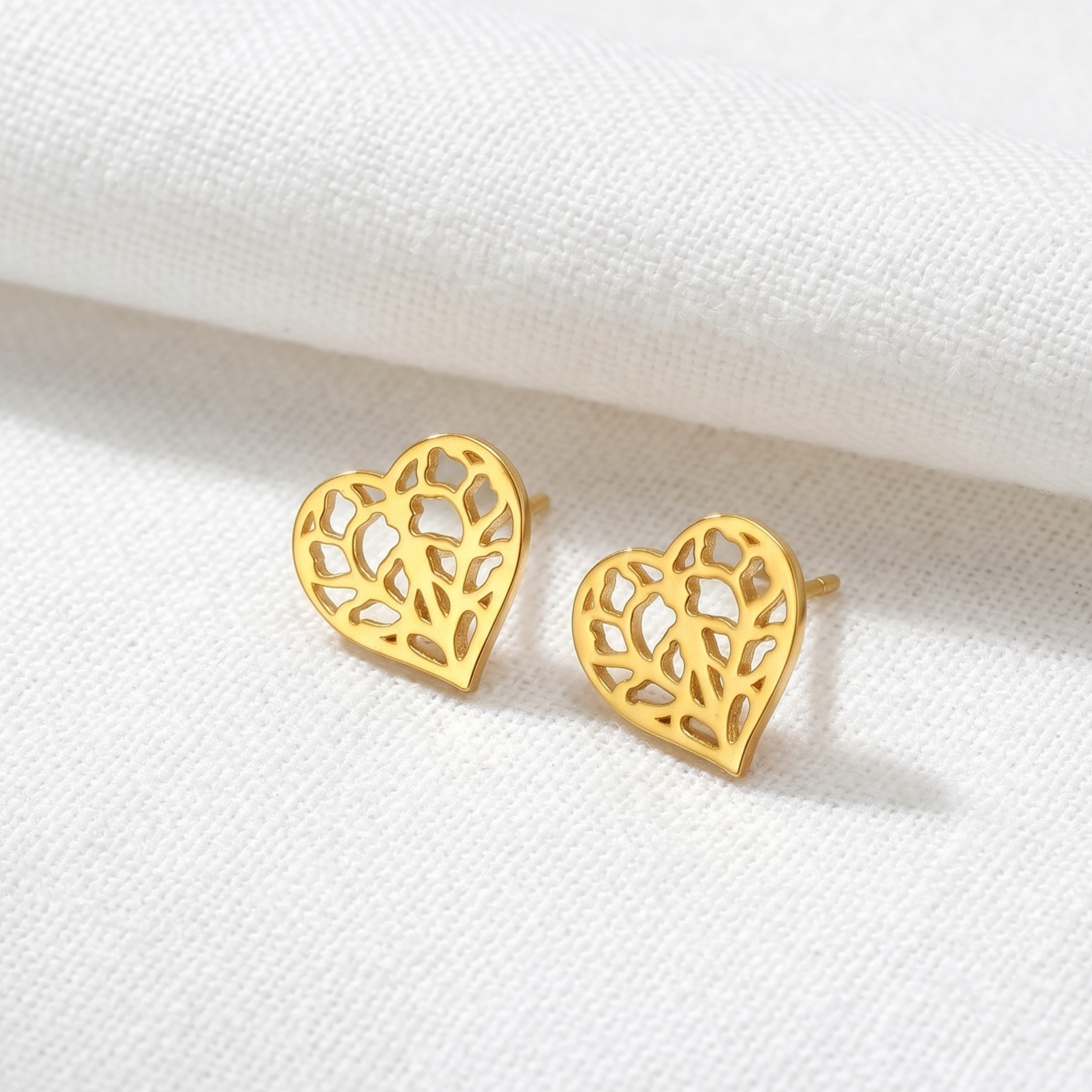 Pair of gold vermeil heart-shaped stud earrings with detailed openwork floral motifs inspired by Yorkshire, resting on textured brown fabric background.