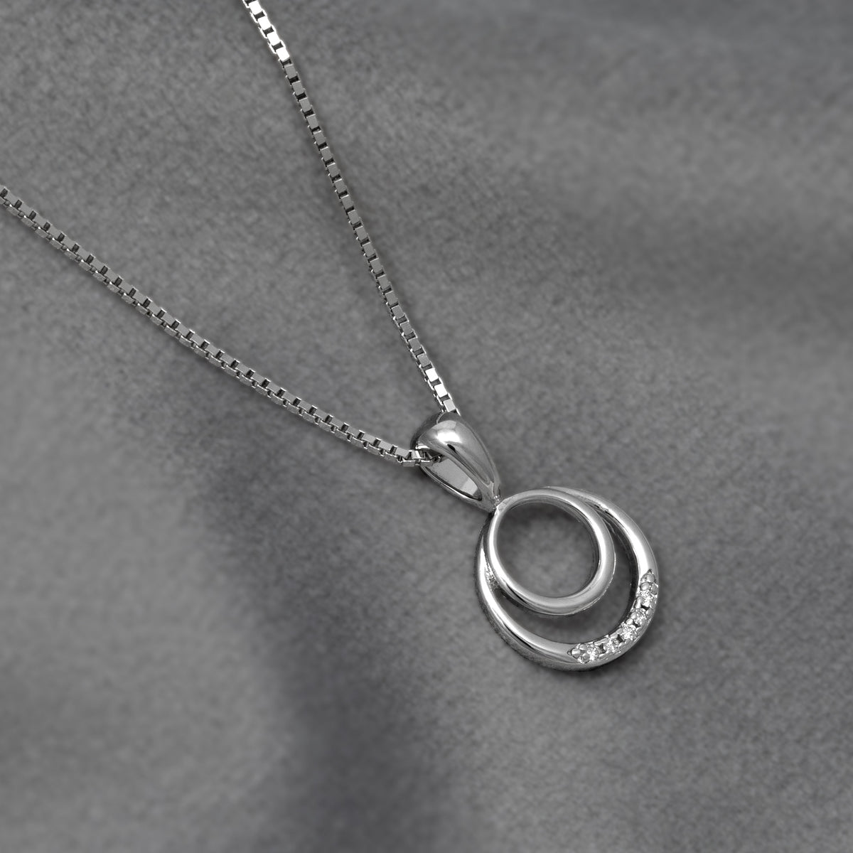 Sterling silver pendant featuring two interlocking circles, one accented with 0.02 carat lab grown diamonds, suspended from a fine box chain on a soft grey textured background.