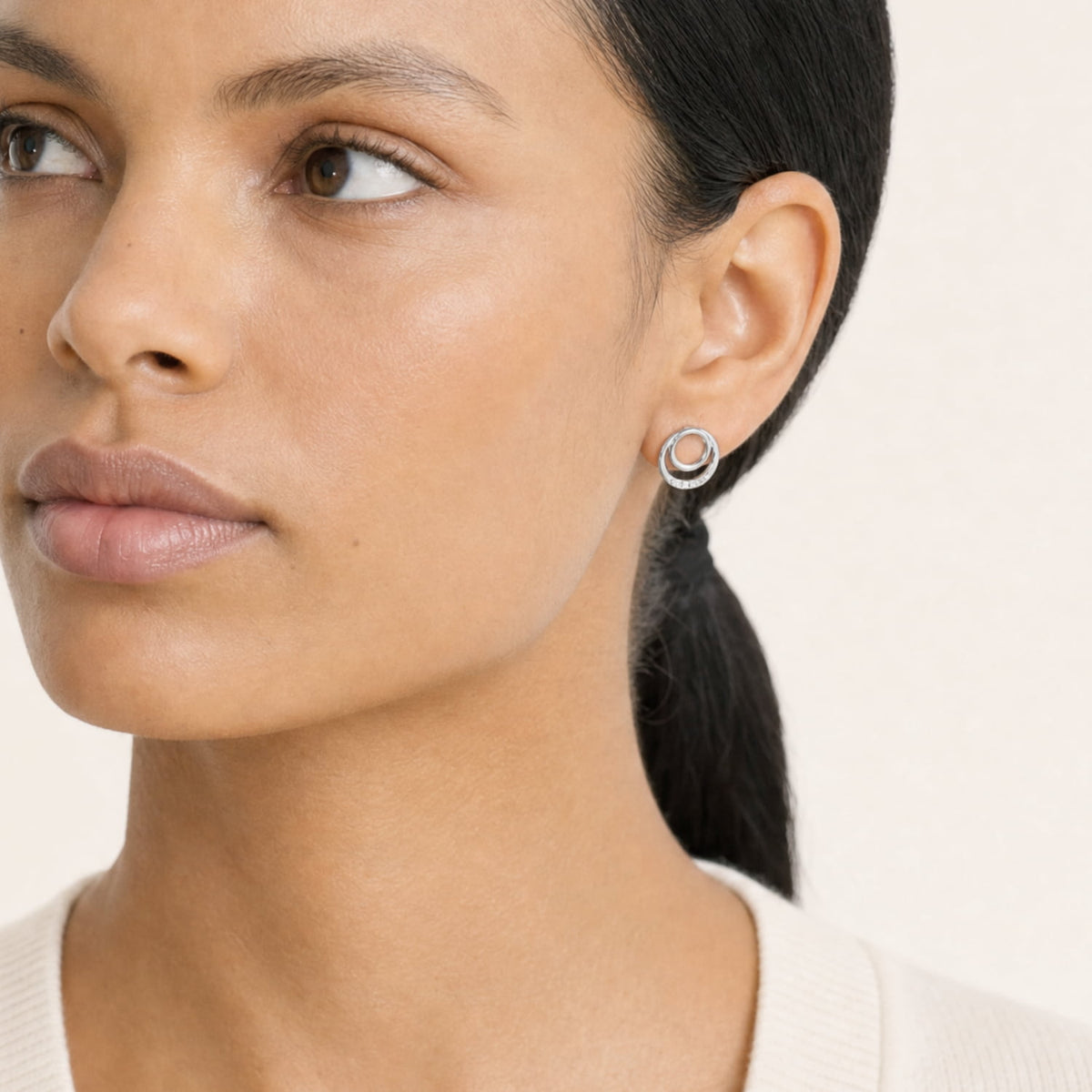 Model wears sterling silver stud earrings featuring two interlocking circles accented with three small lab grown diamonds, offering a minimalist and modern design.