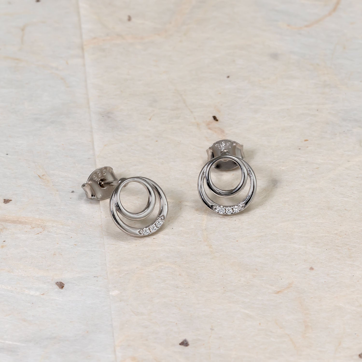 Pair of sterling silver stud earrings featuring two intertwined open circles accented with a row of small sparkling lab grown diamonds, showcasing modern sculptural design.