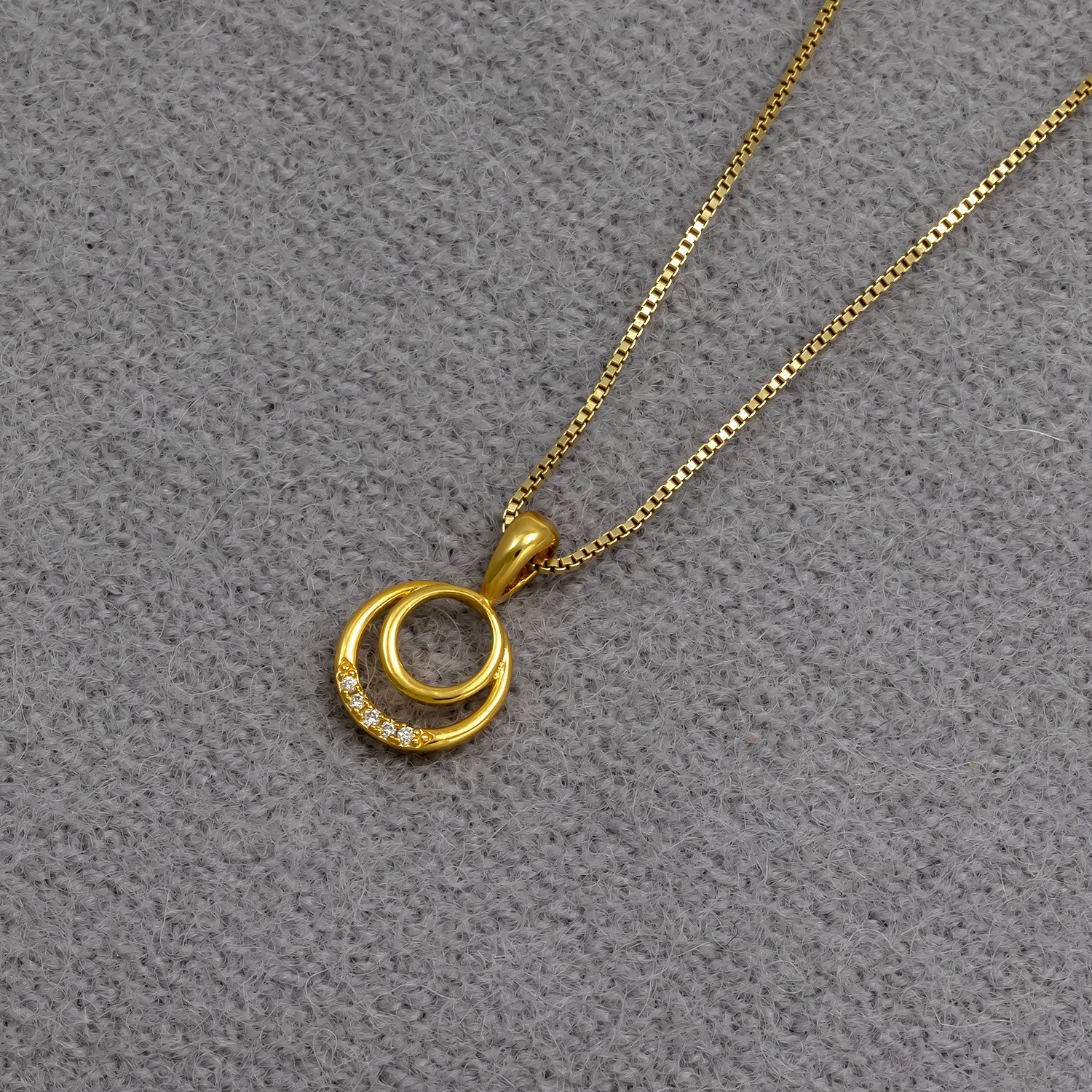 Gold vermeil pendant necklace featuring two interlocking circles, one adorned with small lab grown diamonds, suspended from a fine gold chain on a neutral grey fabric.