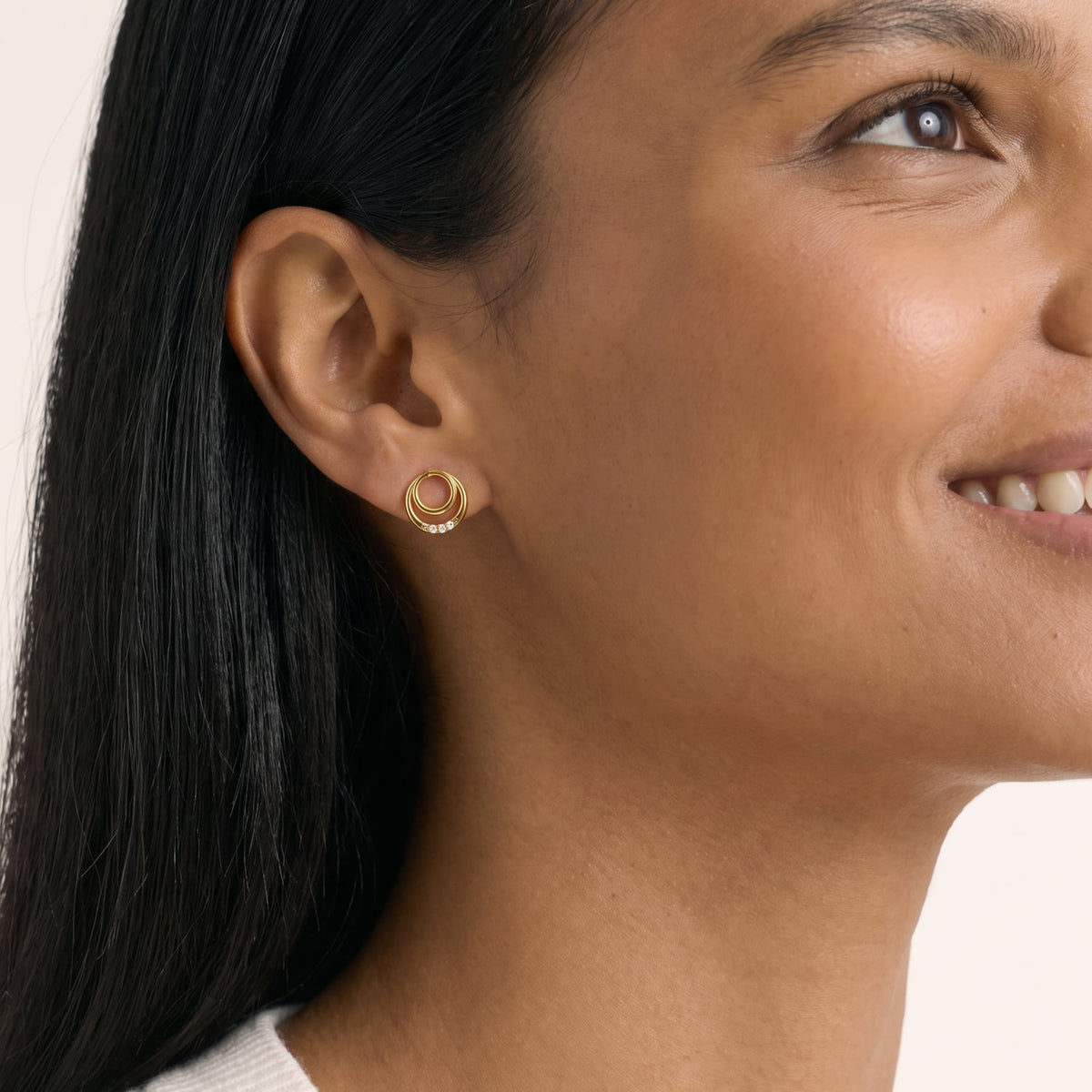 Model wears a pair of gold vermeil stud earrings featuring interlocking double circles accented with a row of lab grown diamonds, showcasing a sleek and modern design.