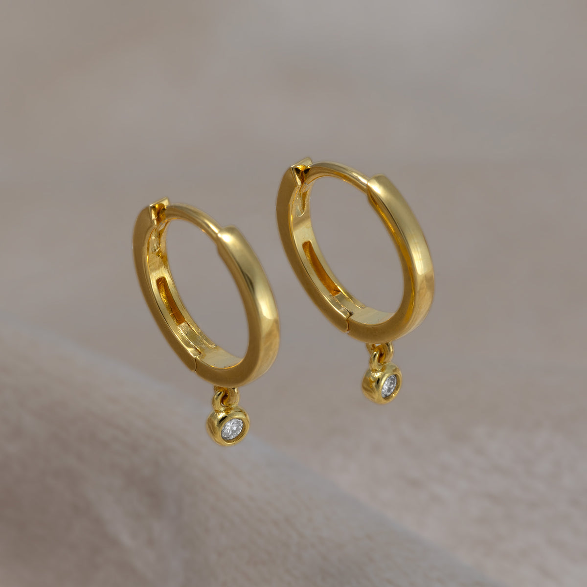 Pair of gold vermeil hinged hoop earrings featuring small round lab grown diamond charms, displayed on a soft cream textured fabric surface.