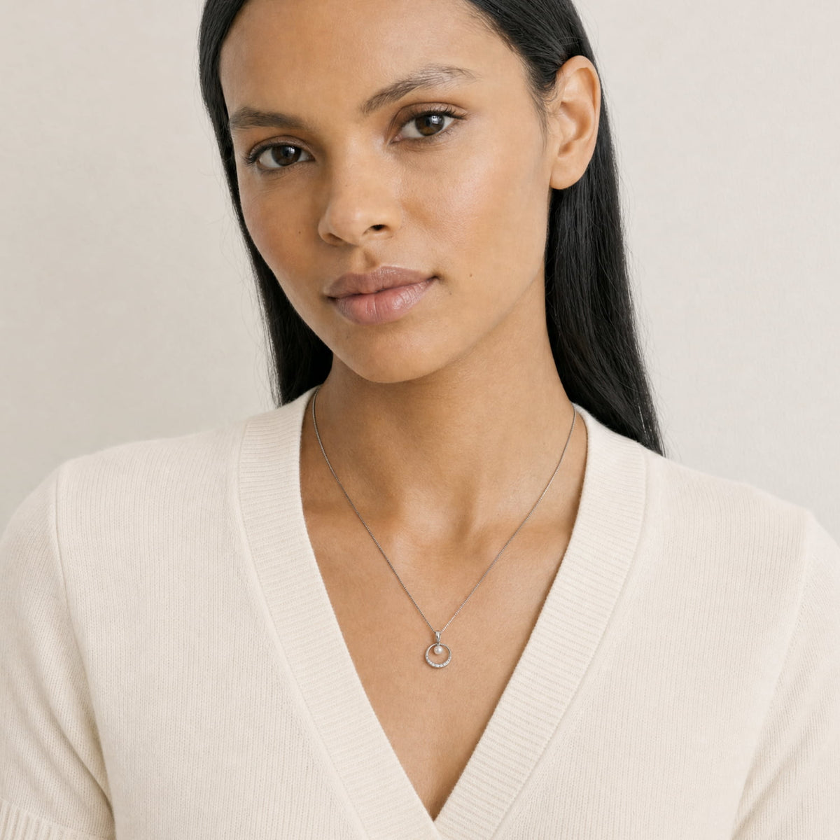 A woman wears a sterling silver pendant necklace featuring a circular design accented with a freshwater pearl and small lab-grown diamonds, suspended from a fine chain.