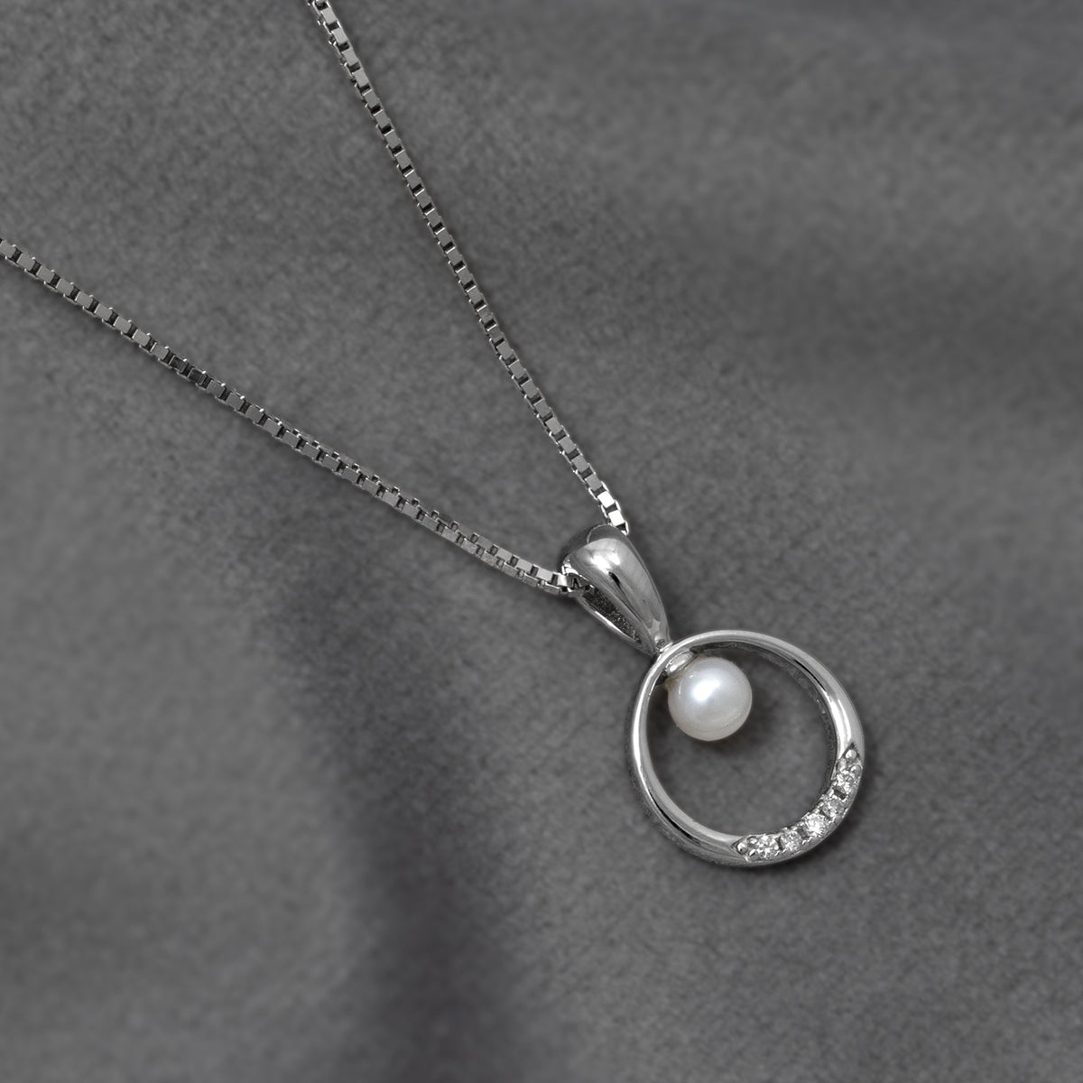 Elegant sterling silver necklace featuring a sculptural circle pendant accented with a freshwater pearl and a row of sparkling lab-grown diamonds, resting on a soft grey fabric background.